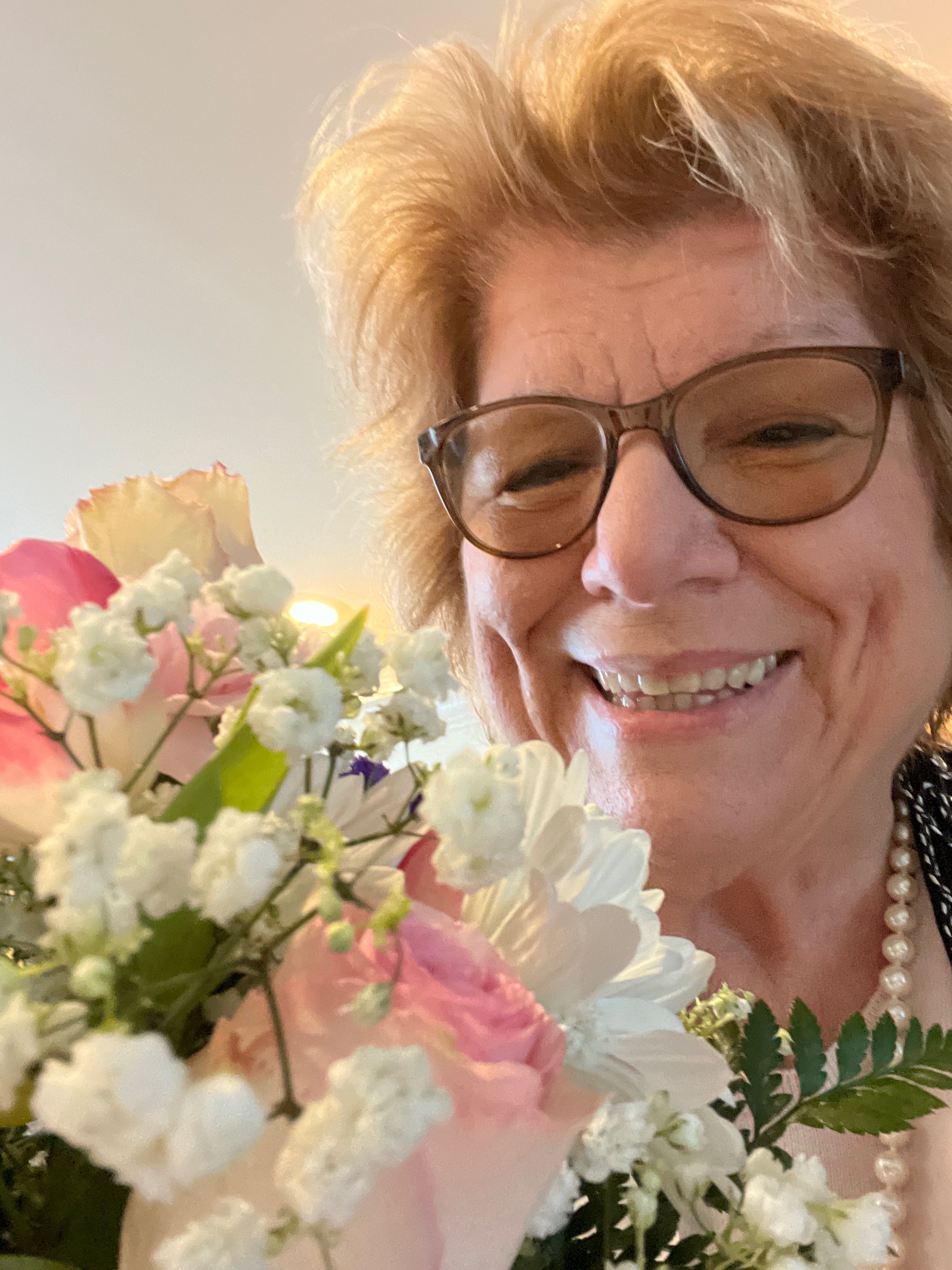 Mom smiling, wearing glasses and holding birthday roses pink and white