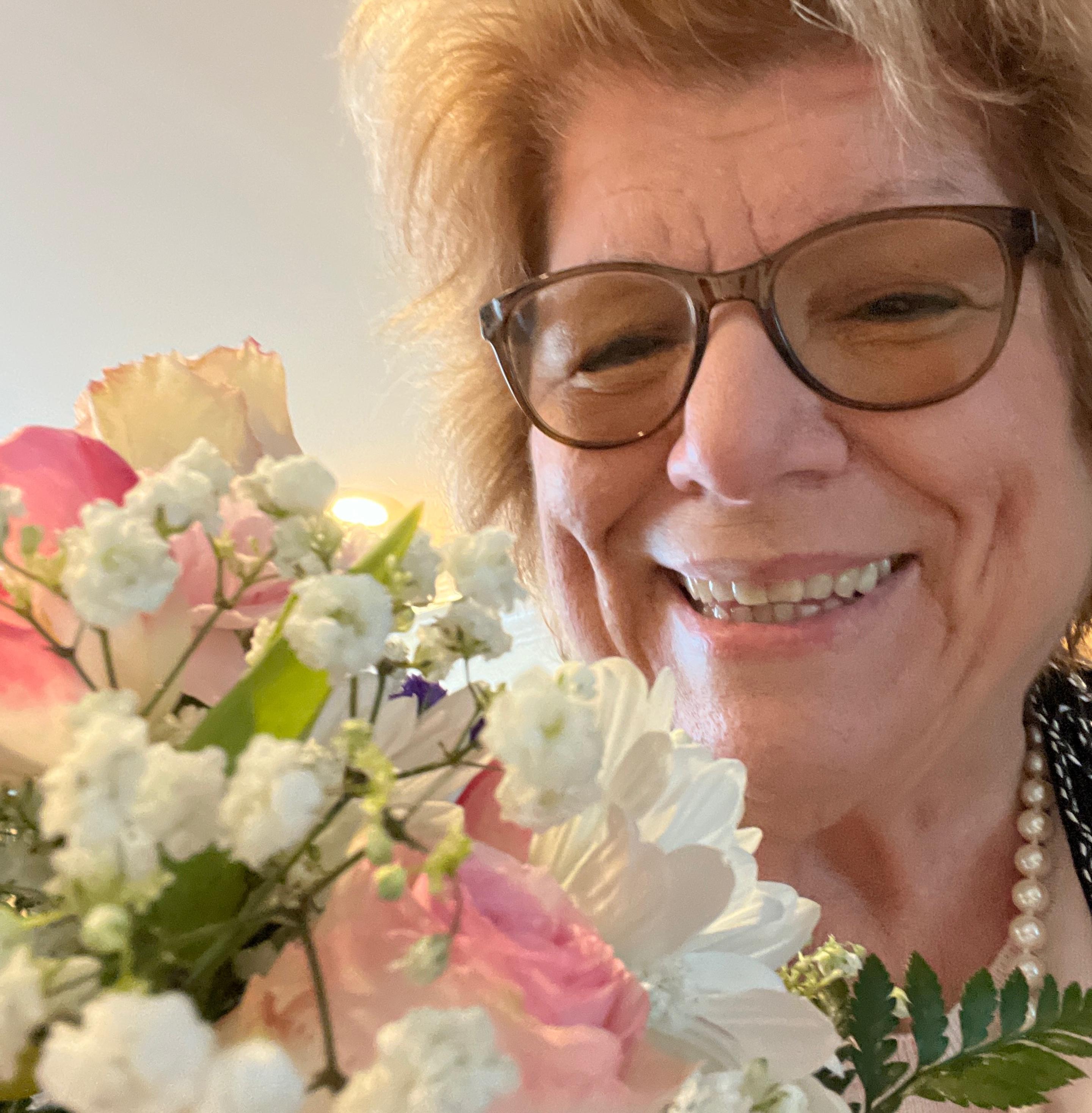 Mom smiling, wearing glasses and holding birthday roses pink and white