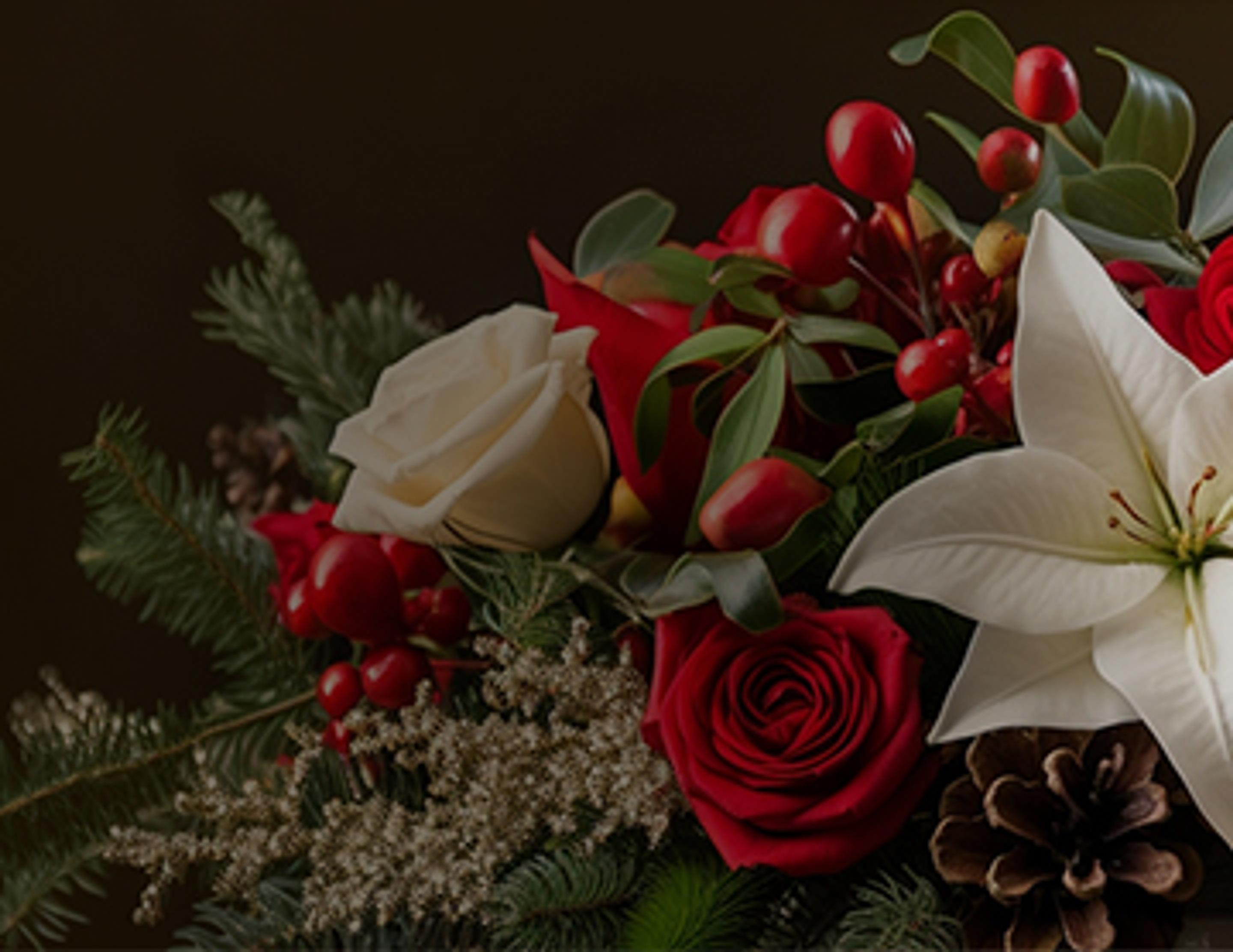 Holiday-themed floral arrangement with red roses, white roses, and holly.
