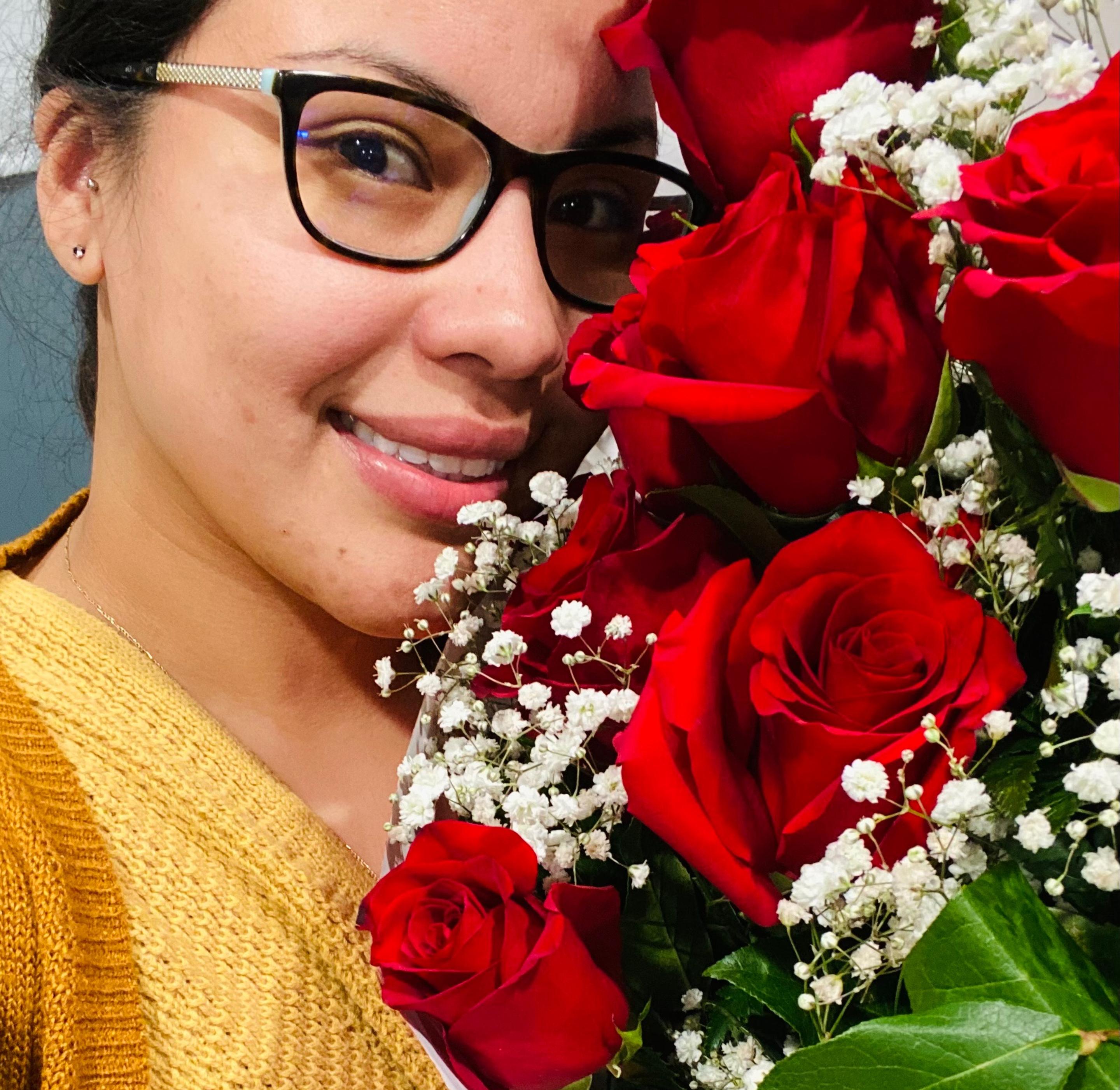 Contented woman with glasses posing with a vibrant bouquet of red roses and baby's breath for Valentine's Day