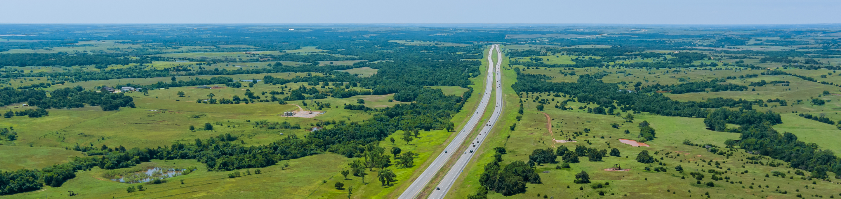 A view of Oklahoma's vast green plains in closeup with a blurred background of fields and highways stretching toward the horizon under a clear blue sky.