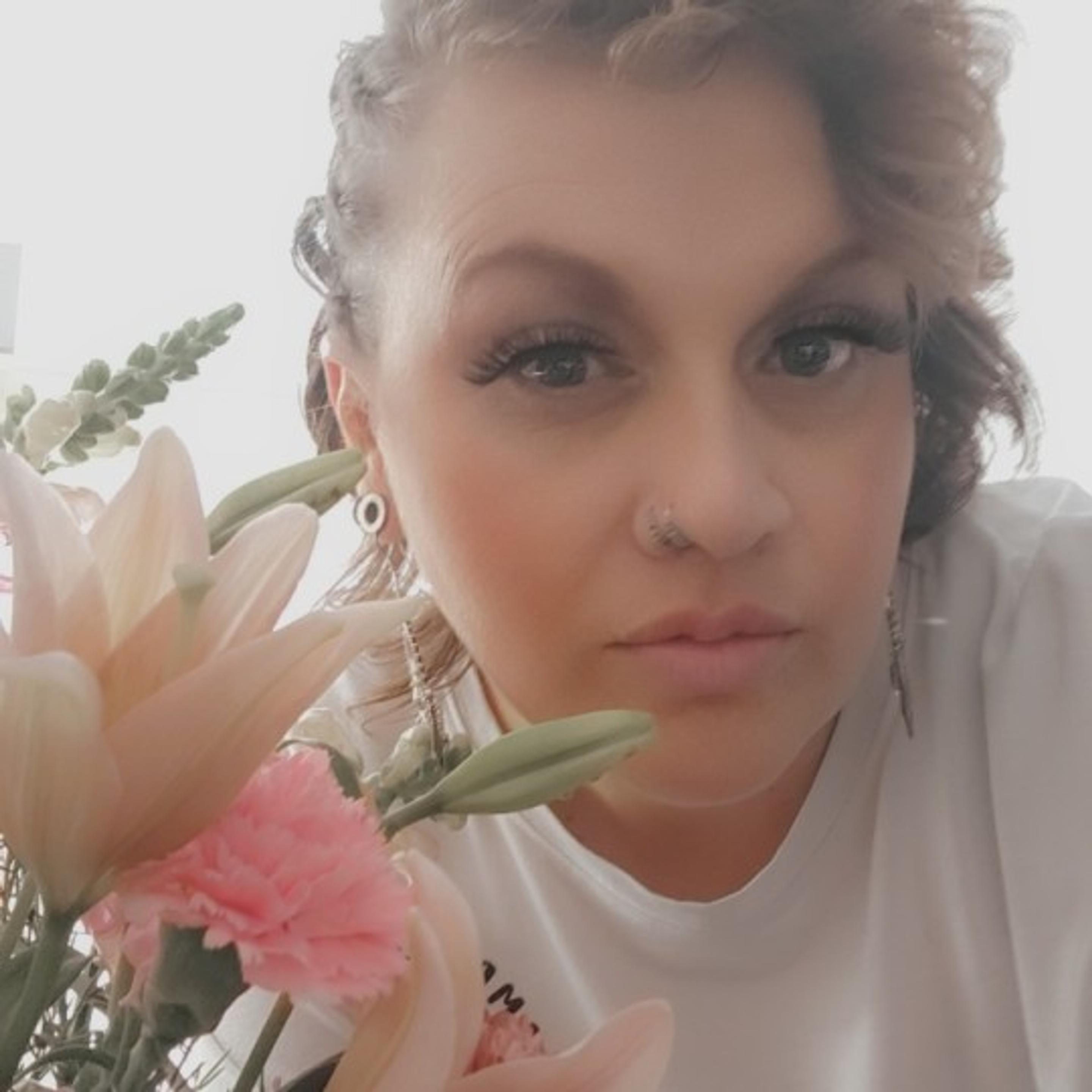 Just Because flowers with woman looking at camera with curly hair, pink flowers, nose ring