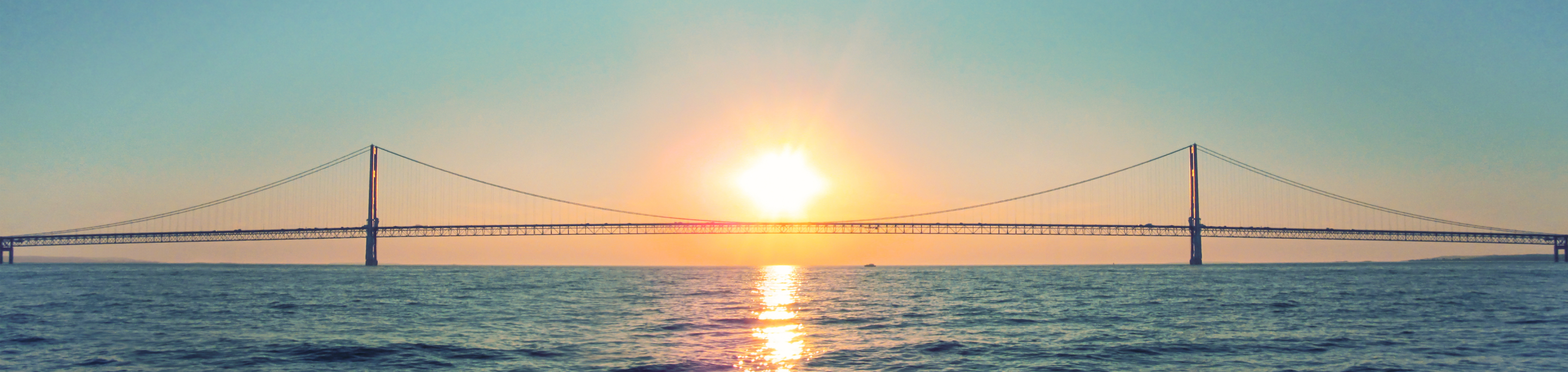 The Mackinac Bridge in closeup with a blurred background of the sun setting over the waters of the Straits of Mackinac in Michigan.