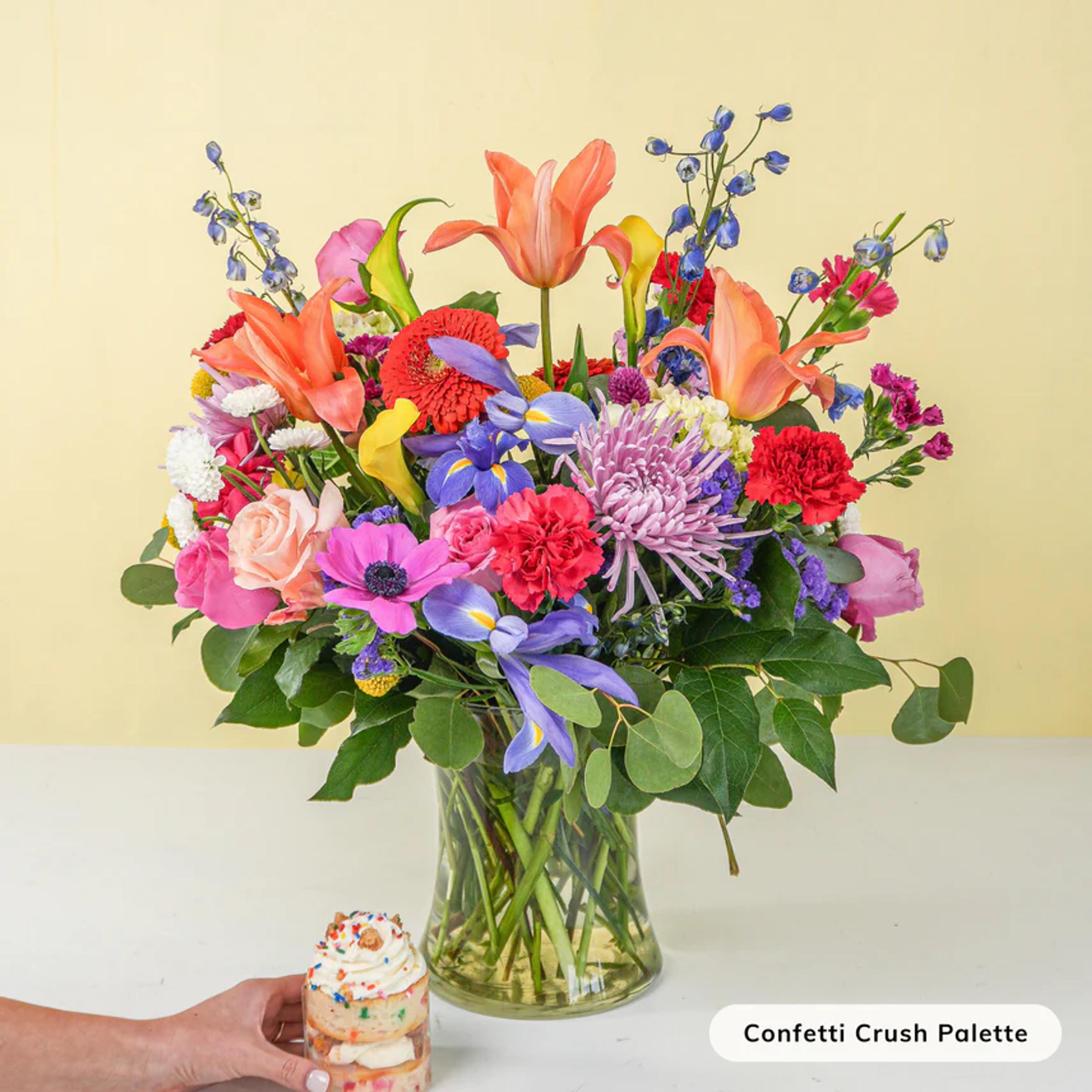 a person is holding a cupcake next to a vase of flowers .