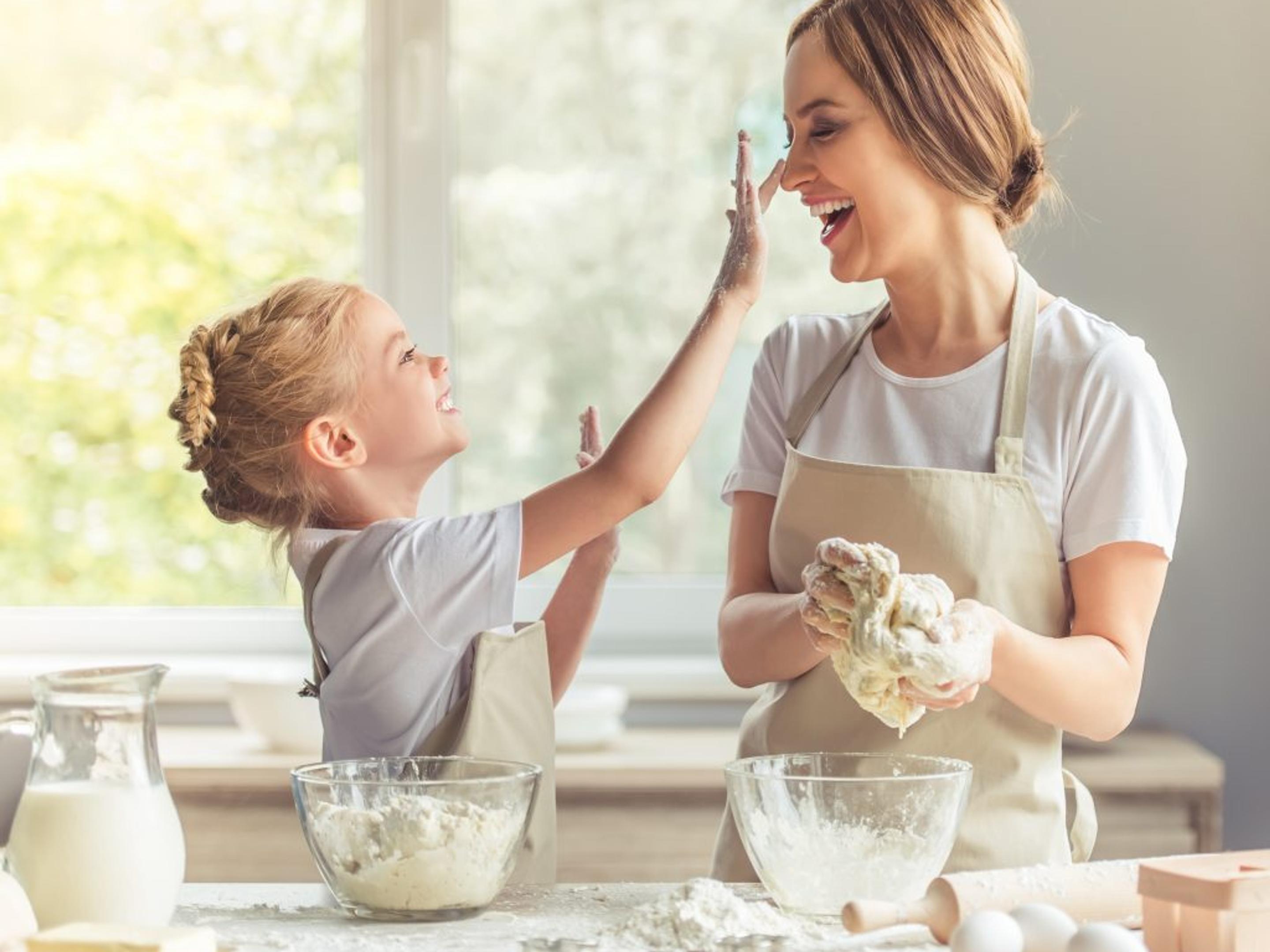 a woman and a little girl are playing with dough in the kitchen .
