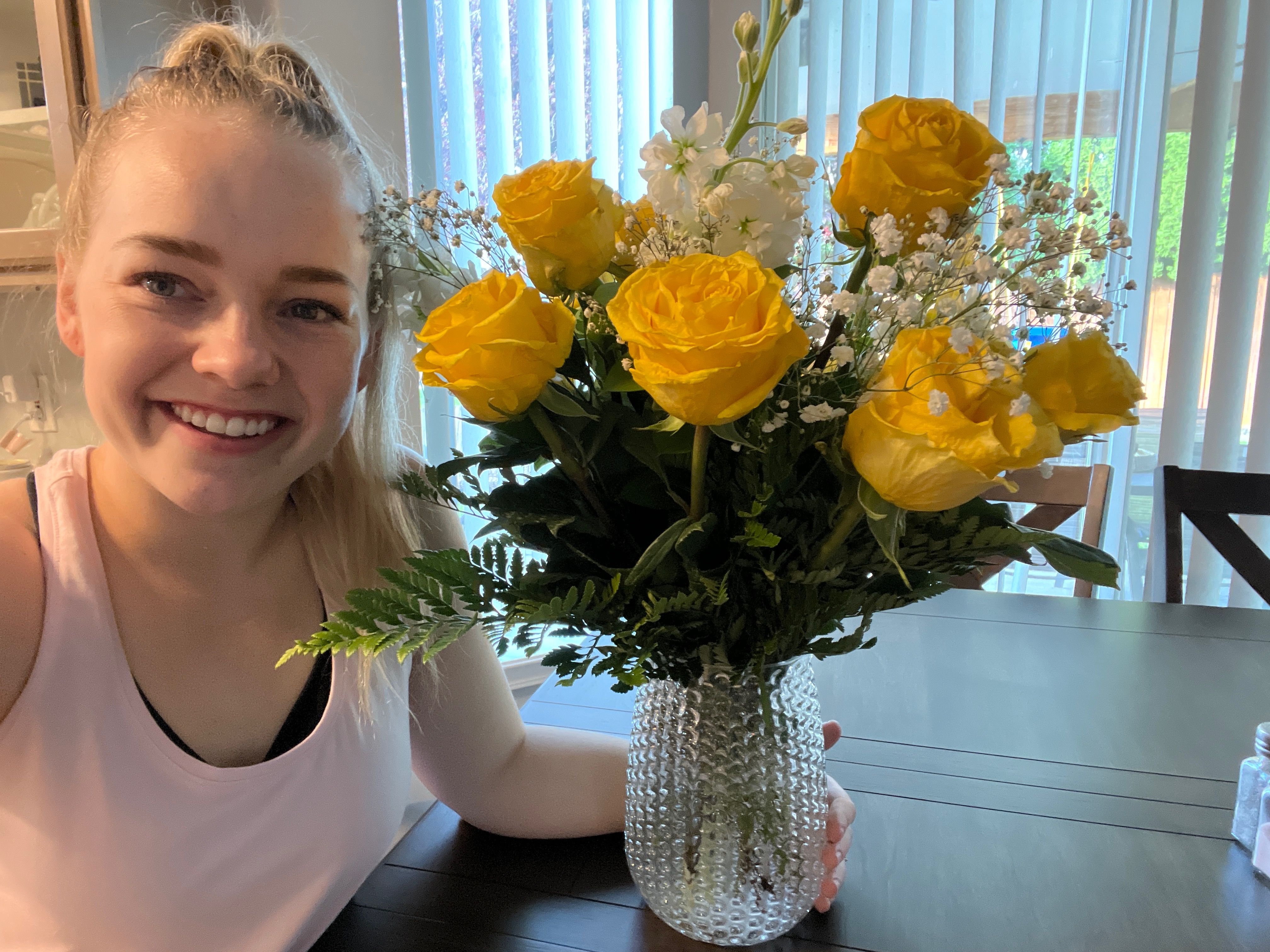 Woman smiling with yellow birthday roses on table in glass vase.