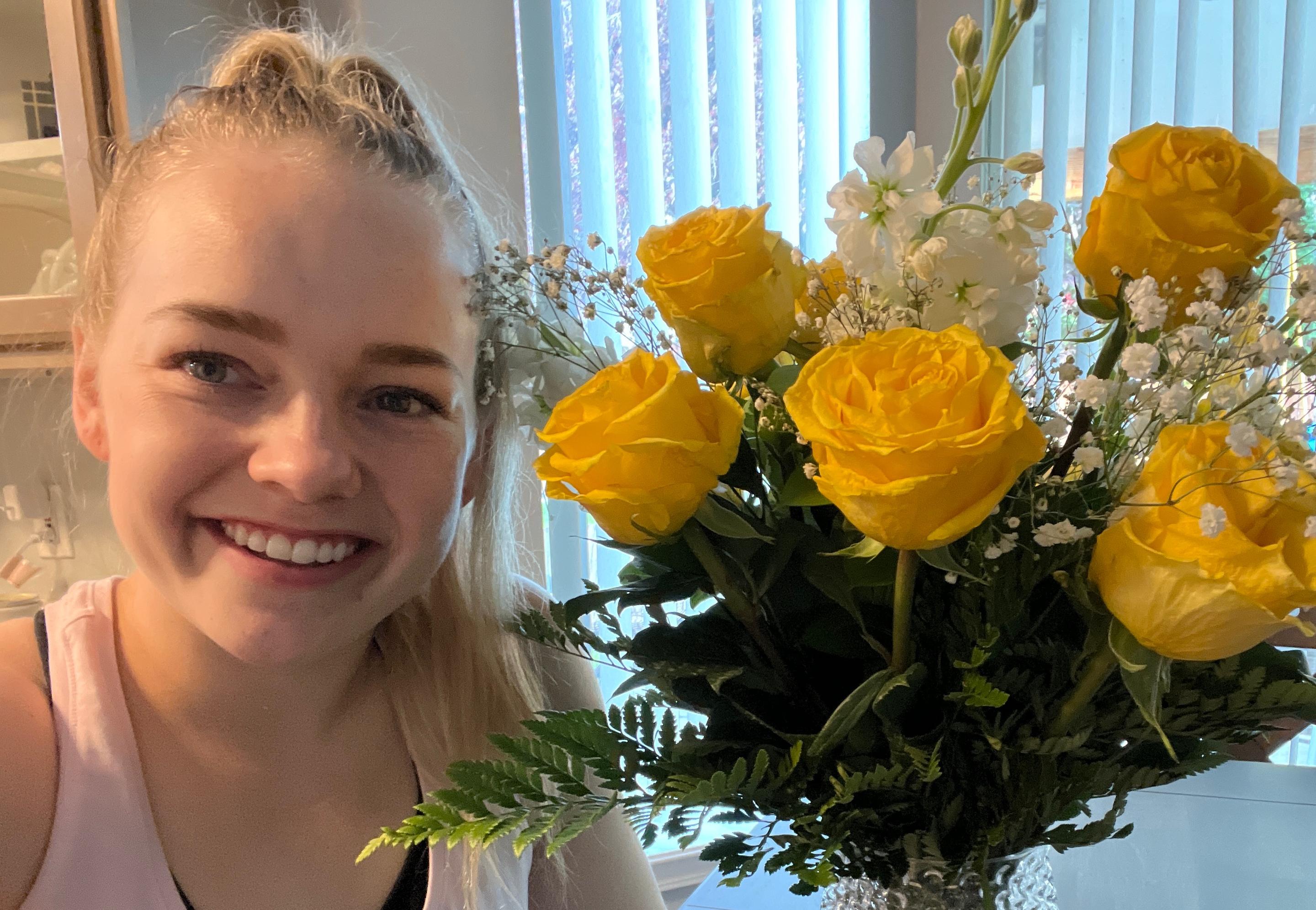 Woman smiling with yellow birthday roses on table in glass vase.
