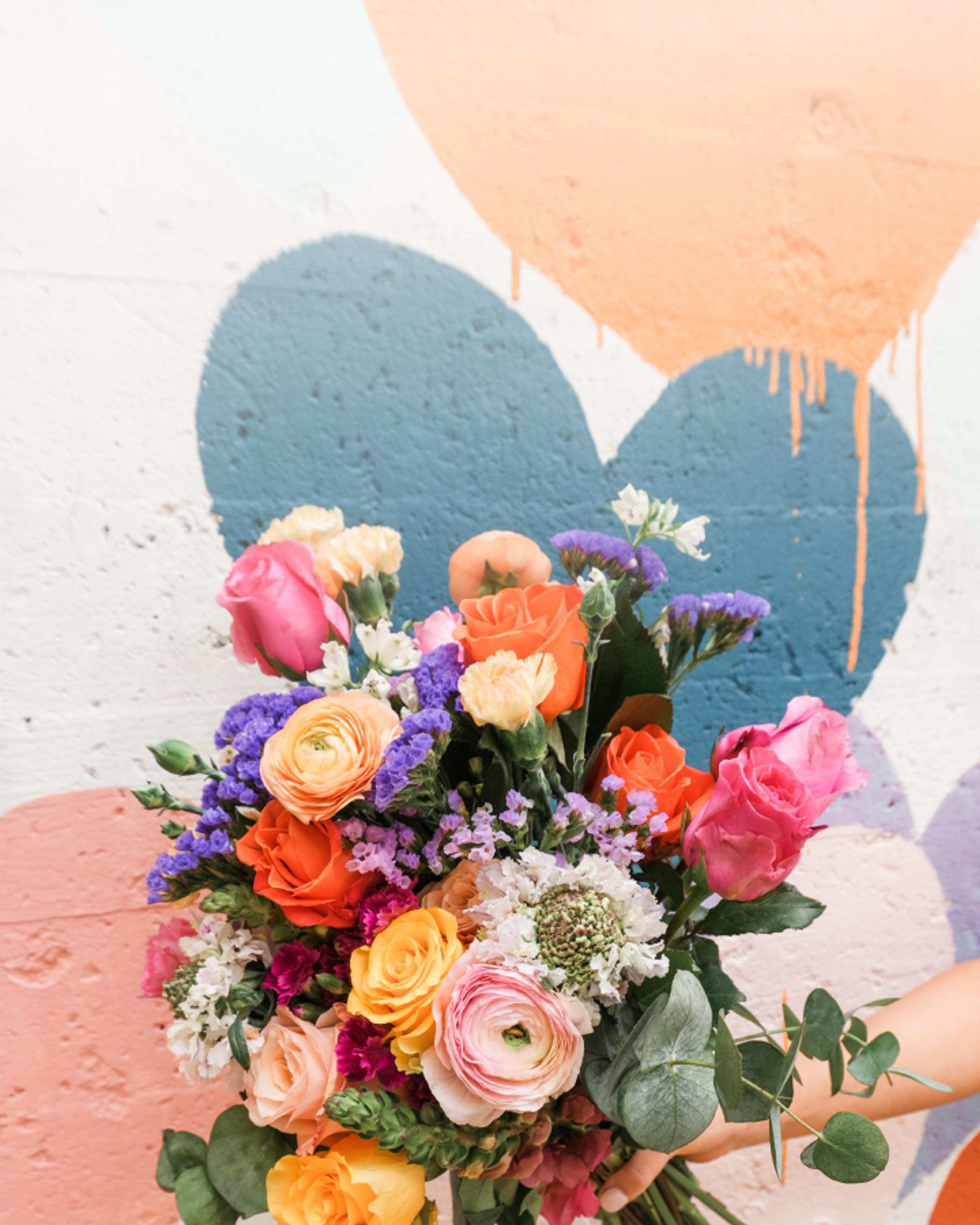 a person is holding a bouquet of colorful flowers in front of a colorful wall .