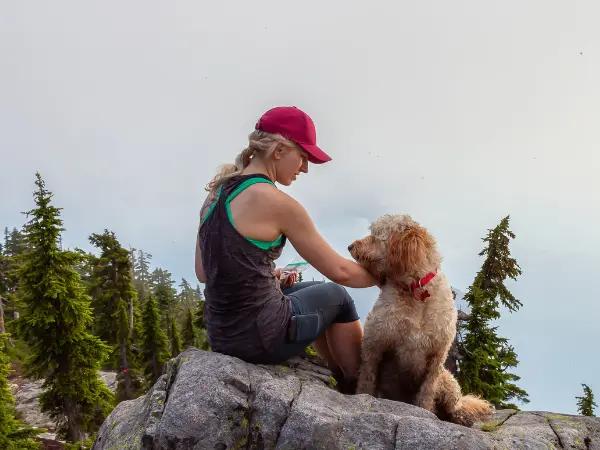 A pet parent and dog sitting on a rock near a forest, representing the experience of exploring dog friendly hikes and trails in Salt Lake City