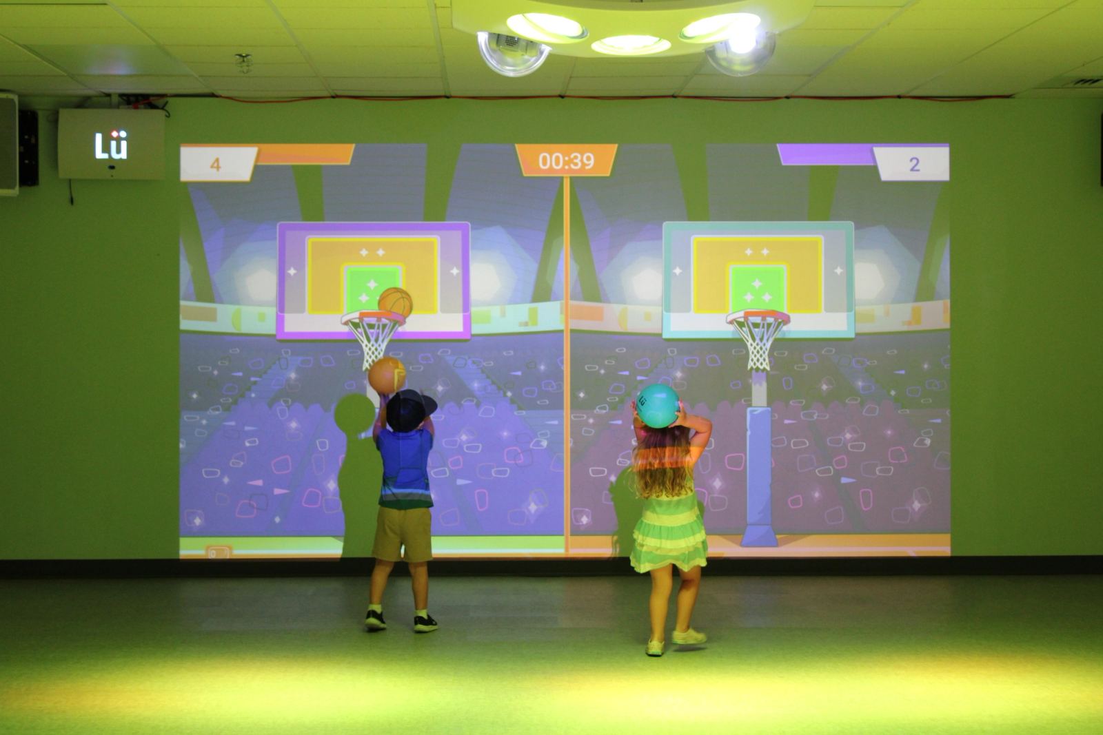 An indoor movement room at SELA's Hingham campus, with an open wood floor, soft-play equipment, and sport wall art.
