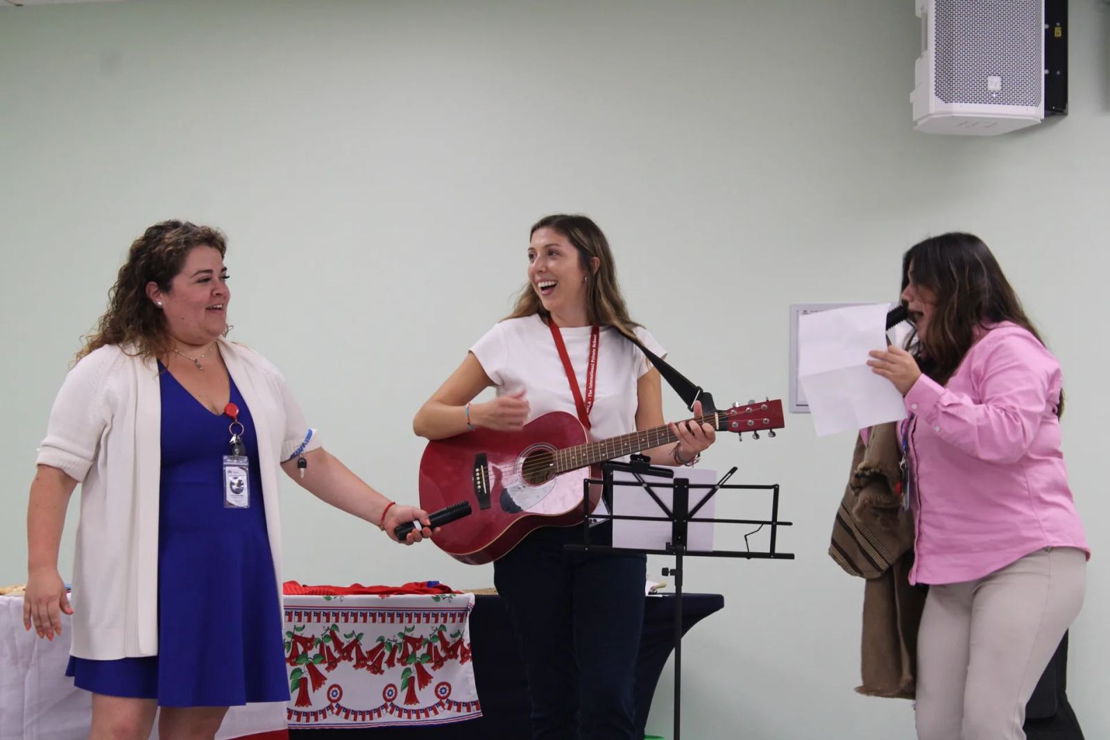 Three SELA teachers perform live music together, one playing guitar and singing, during a school celebration.