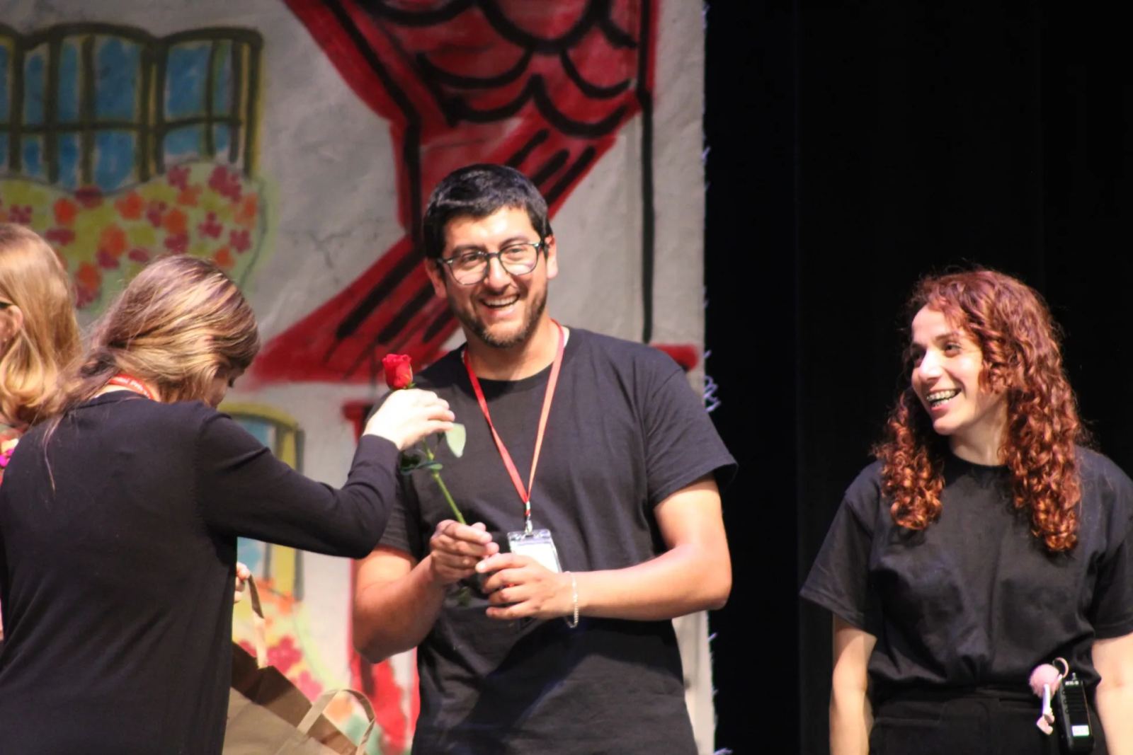 A smiling SELA performer is handed a single red rose on stage on opening night.