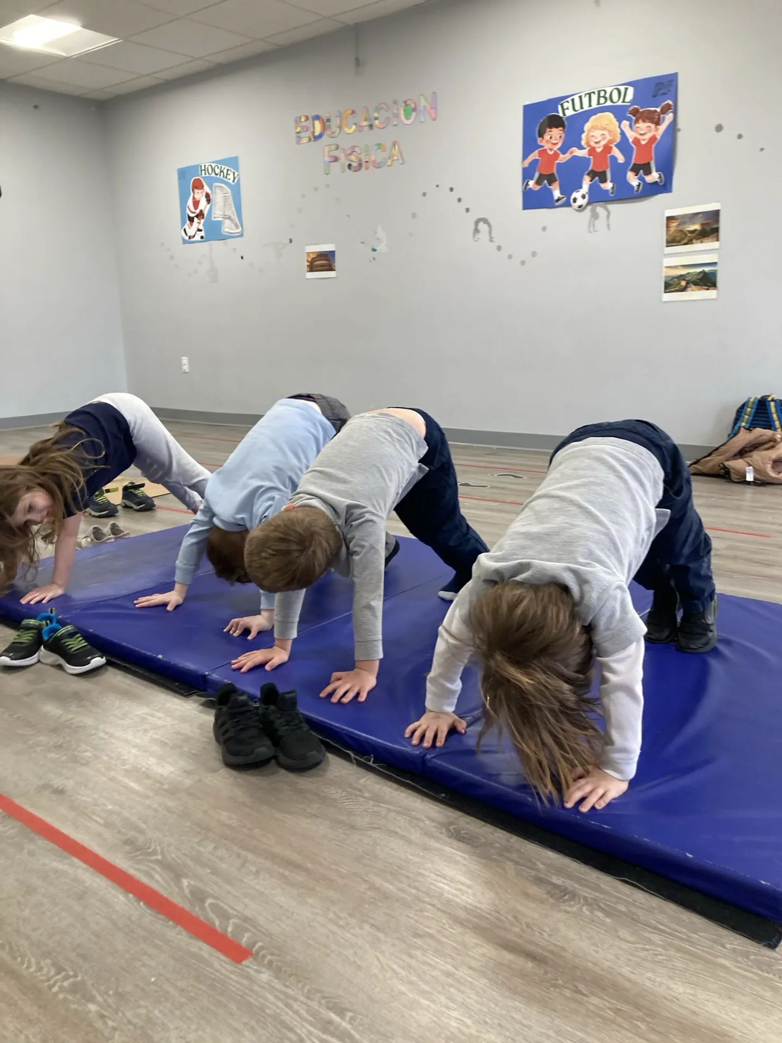 A row of SELA children hold a downward-dog yoga pose on a blue mat in the movement room.