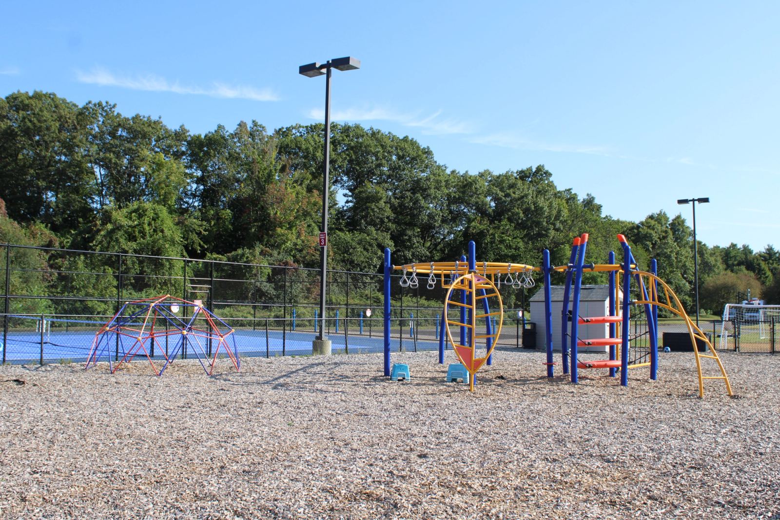 An outdoor playground at SELA's Hingham campus, shaded by a canopy, with a playhouse and climbing structures.