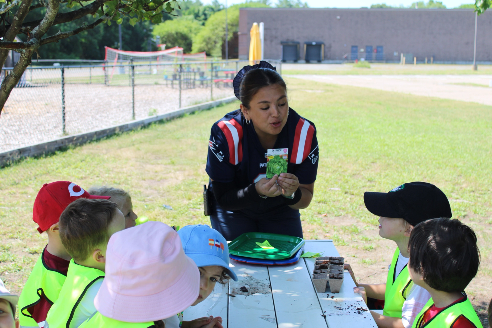 A SELA teacher kneels at a Spanish ‘Calendario’ board, leading a circle of young children in a language lesson.