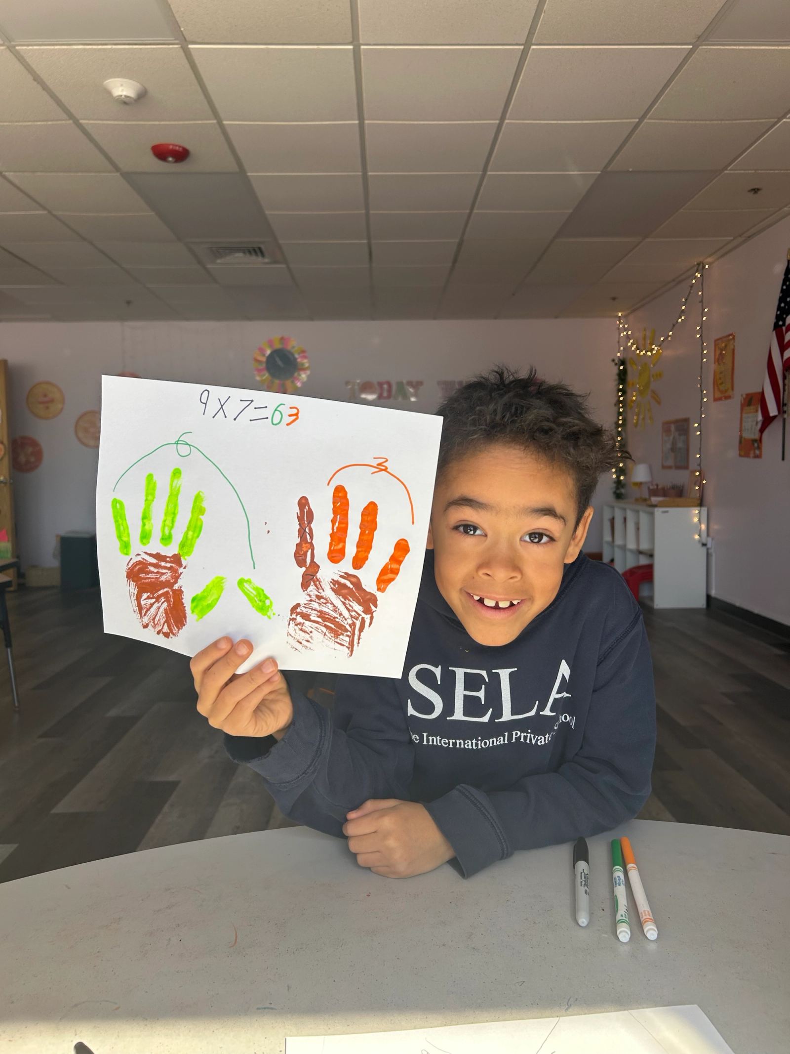 An Upper School student holds up a multiplication problem solved with painted handprints in math class