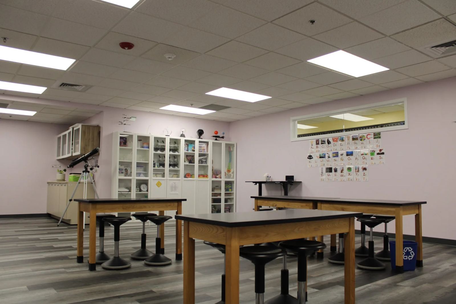 A science lab at SELA's Hingham campus, with black-topped lab tables, stools, a telescope, and equipment cabinets.