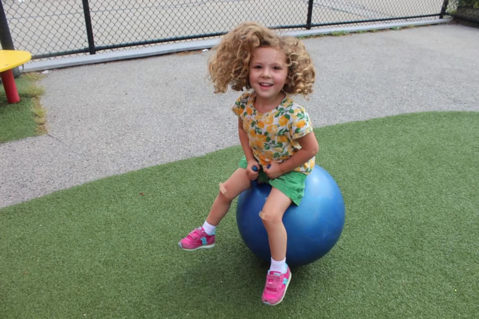 A SELA child bounces on a big blue hopper ball across the green play turf.