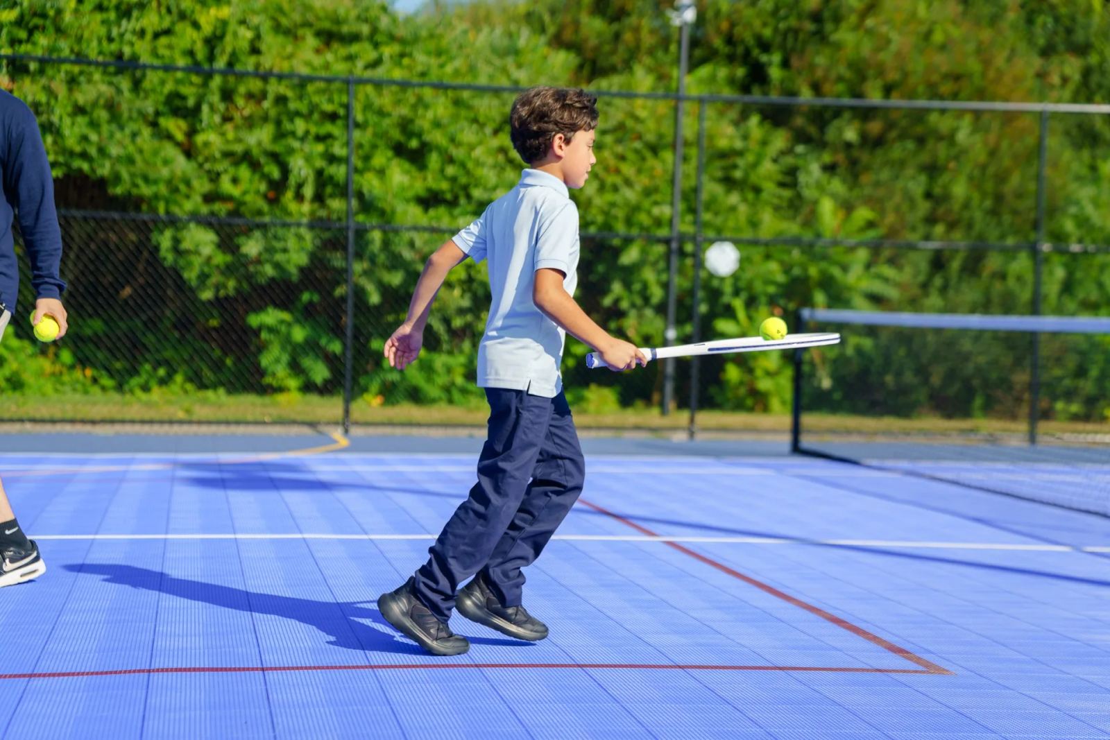 A SELA student returning a ball during a tennis lesson on the outdoor court