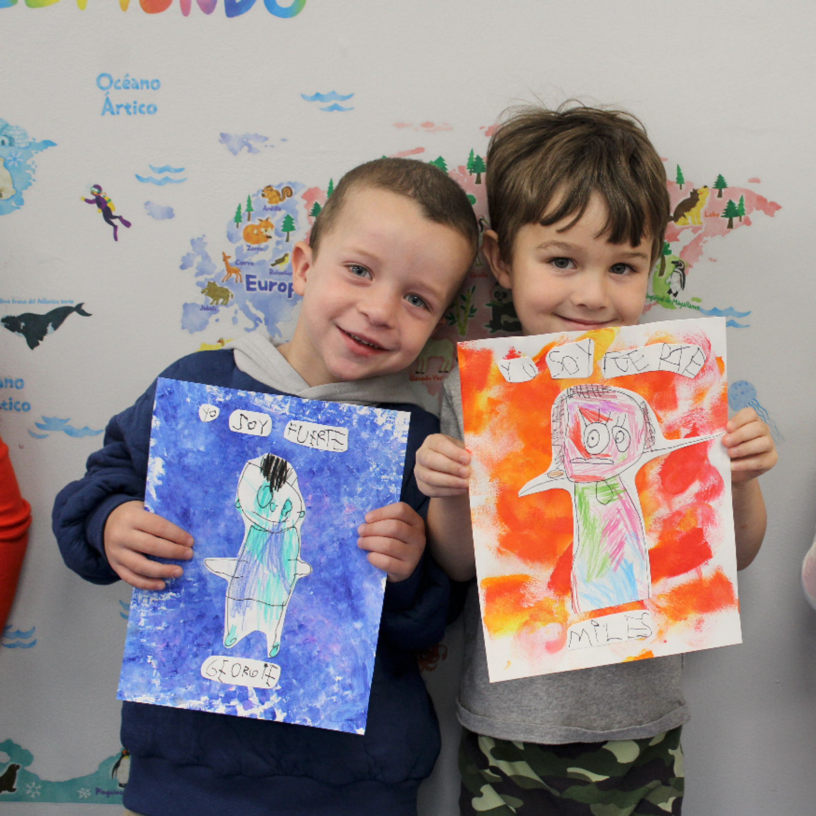 Three SELA preschool students proudly displaying their artwork