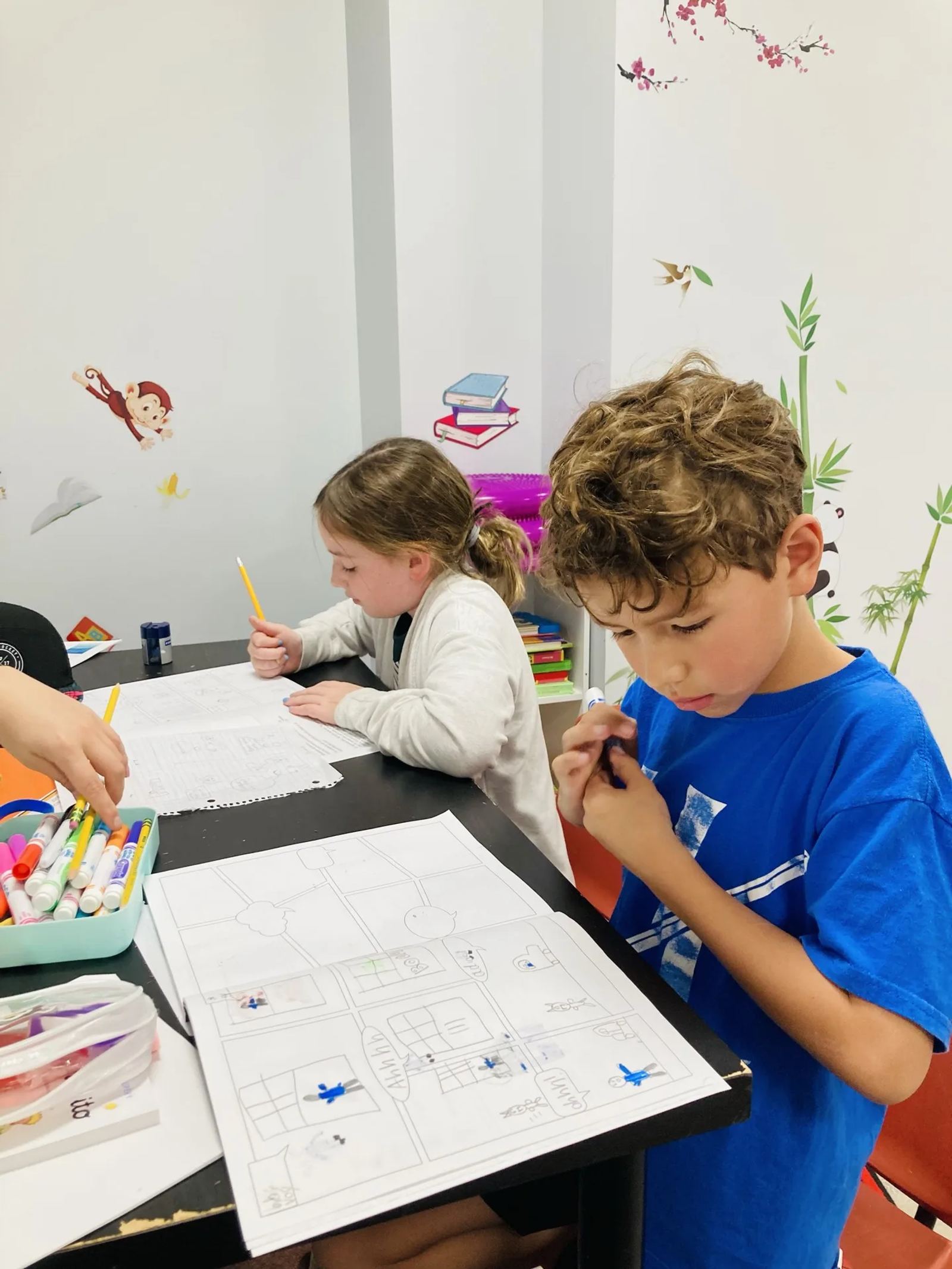 Two SELA students concentrate at a desk, drawing and writing a comic-strip project together.