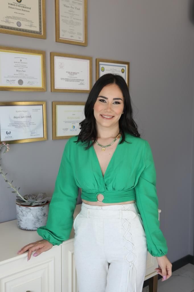 Büşra Sarı Ertek diploma ve sertifikalarının asılı olduğu duvarın önünde
