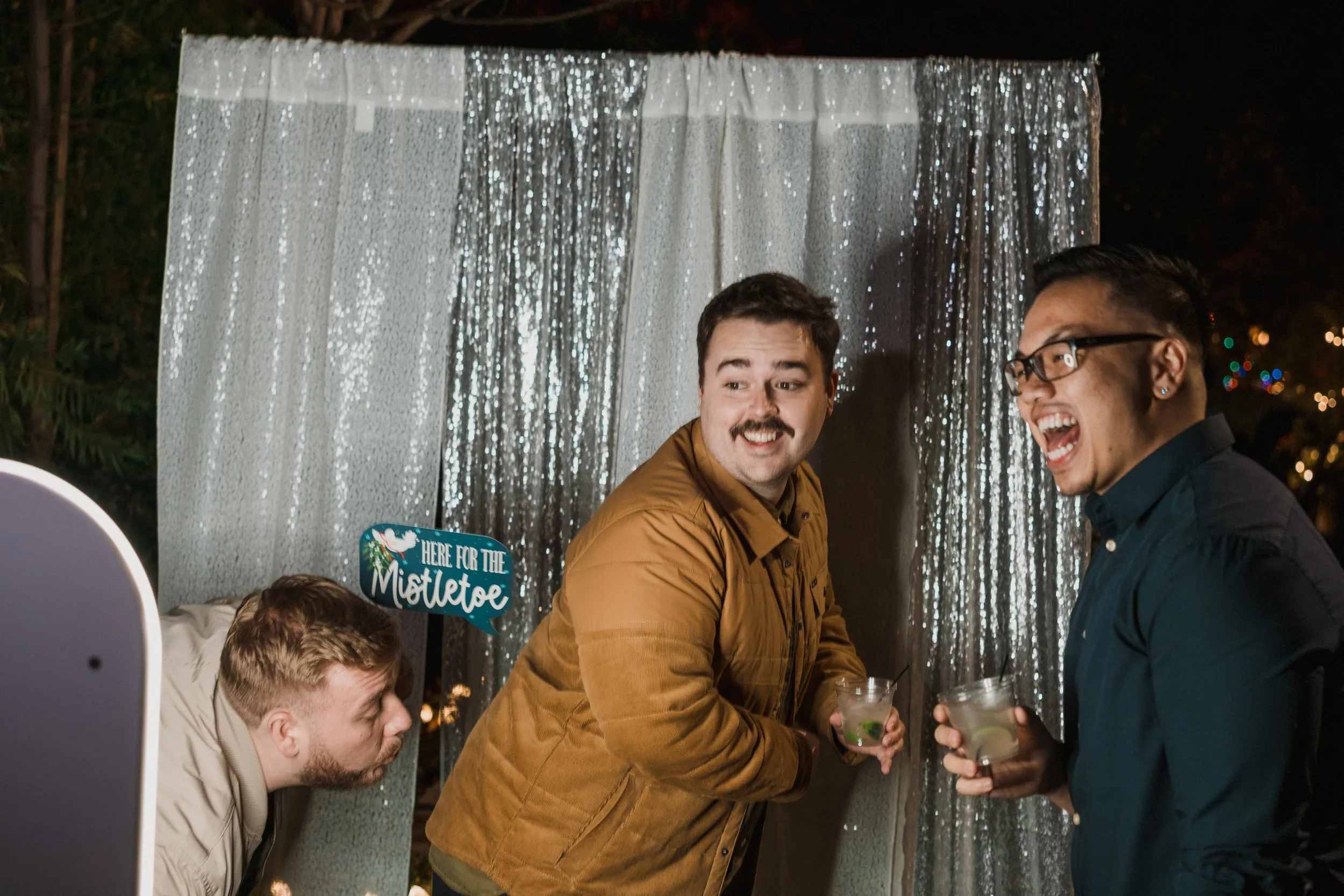 Guests laughing in front of a sequin backdrop at a holiday party, Orange County.