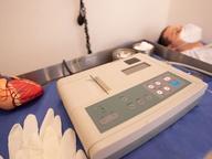 An anatomical heart model beside an electrocardiogram machine in a clinical treatment room.