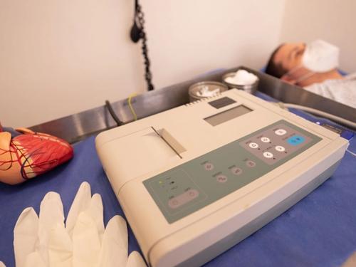 An anatomical heart model beside an electrocardiogram machine in a clinical treatment room.