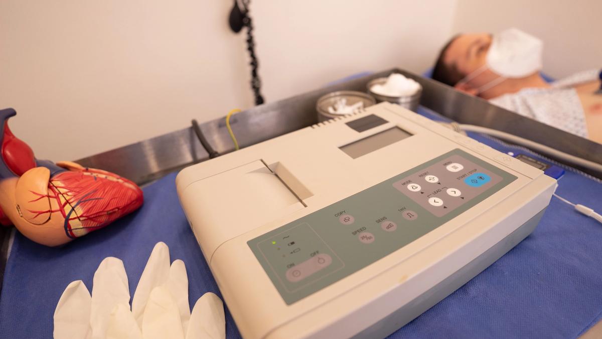 An anatomical heart model beside an electrocardiogram machine in a clinical treatment room.