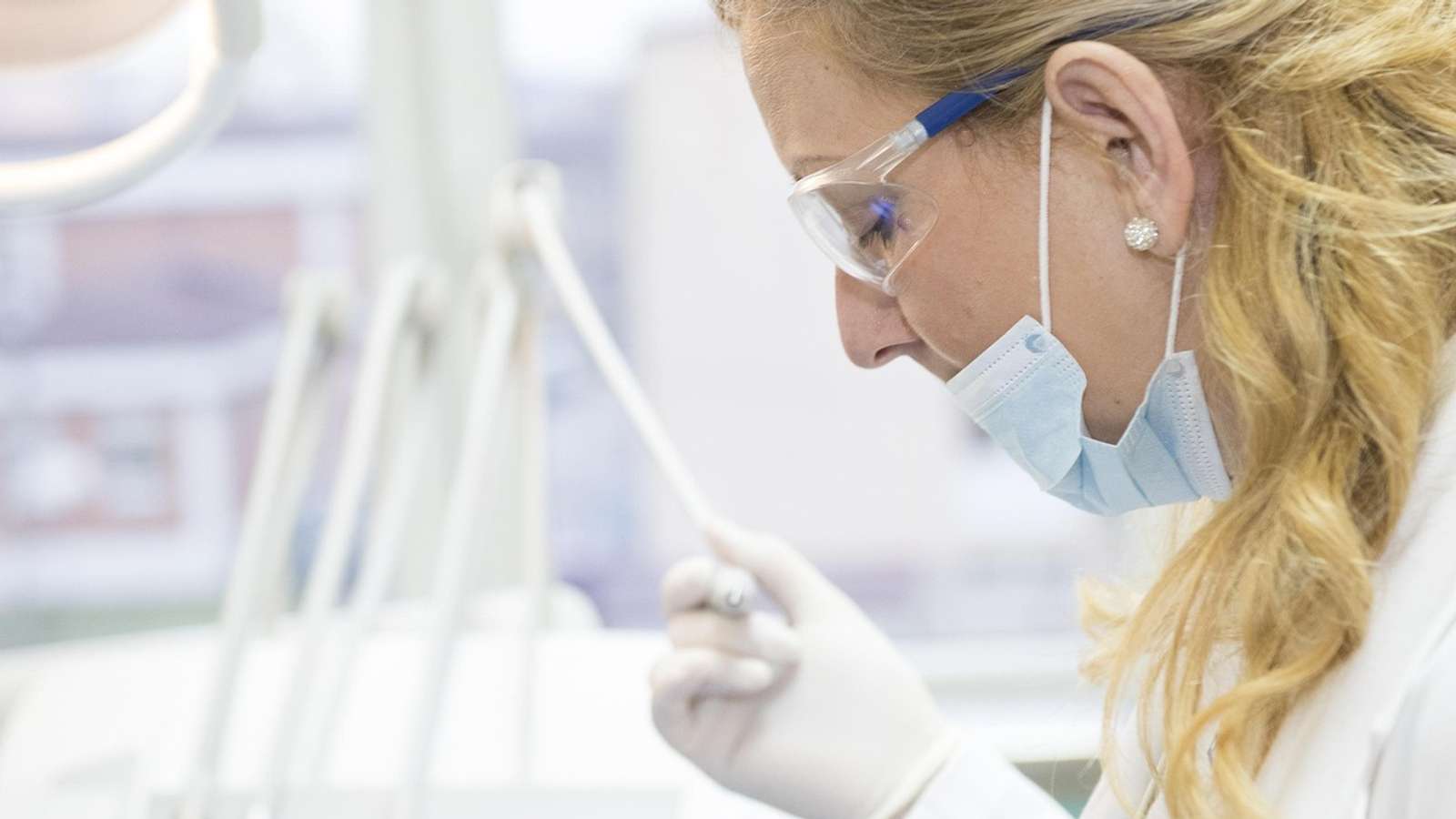 A researcher in gloves and a face mask examining a test tube in a laboratory