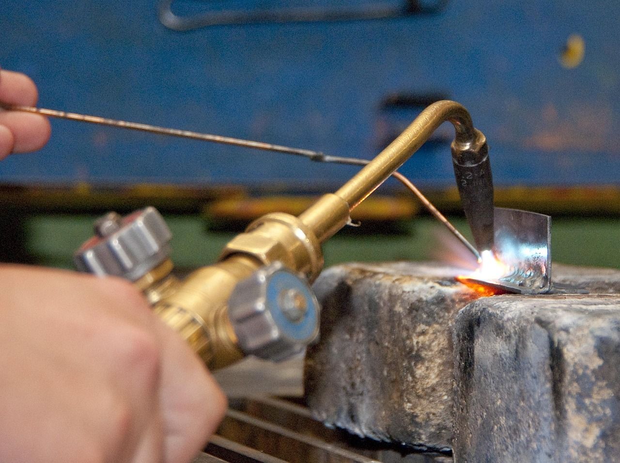 A hand holding a gas torch over a piece of metal in a workshop