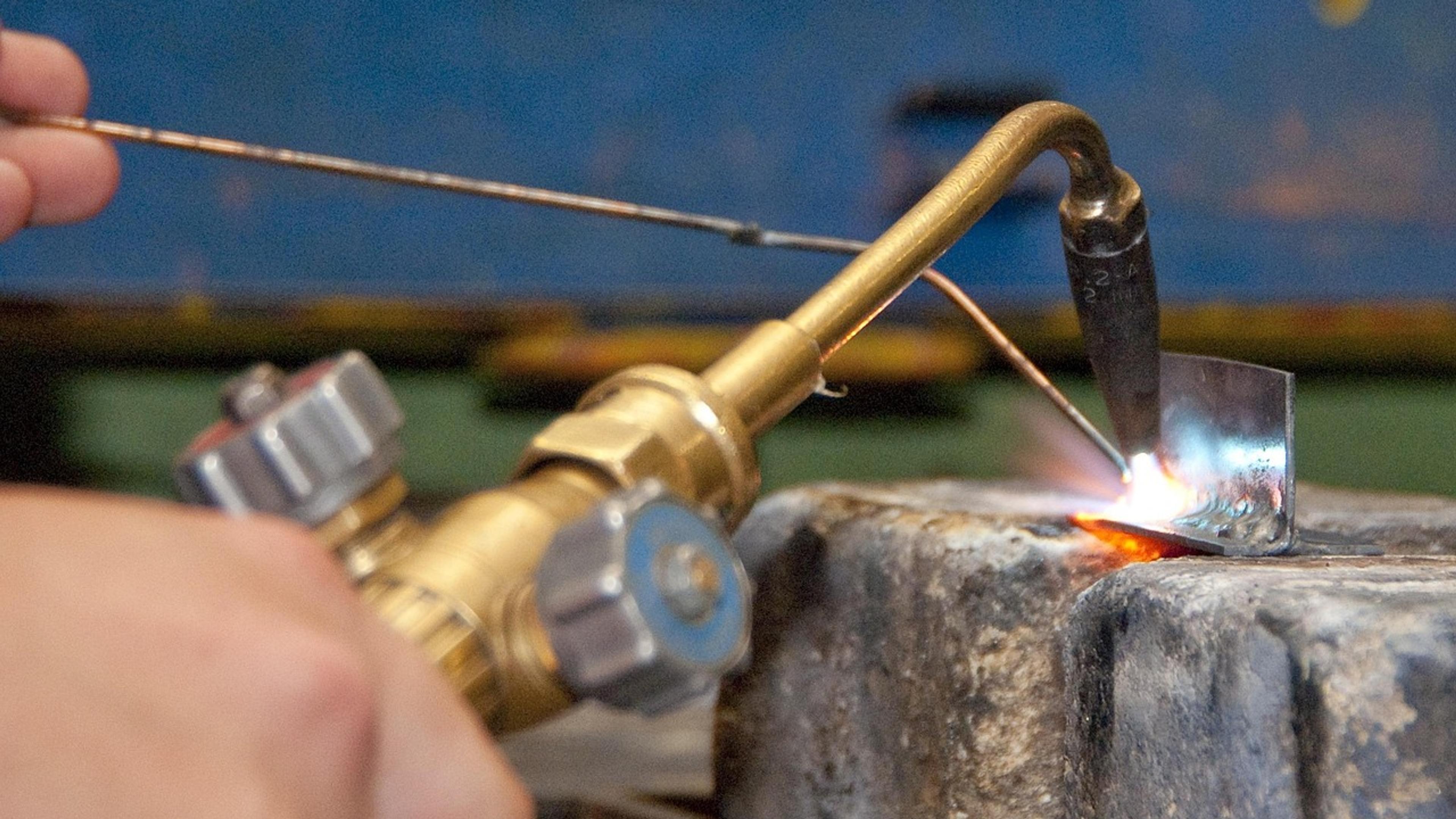 A hand holding a gas torch over a piece of metal in a workshop