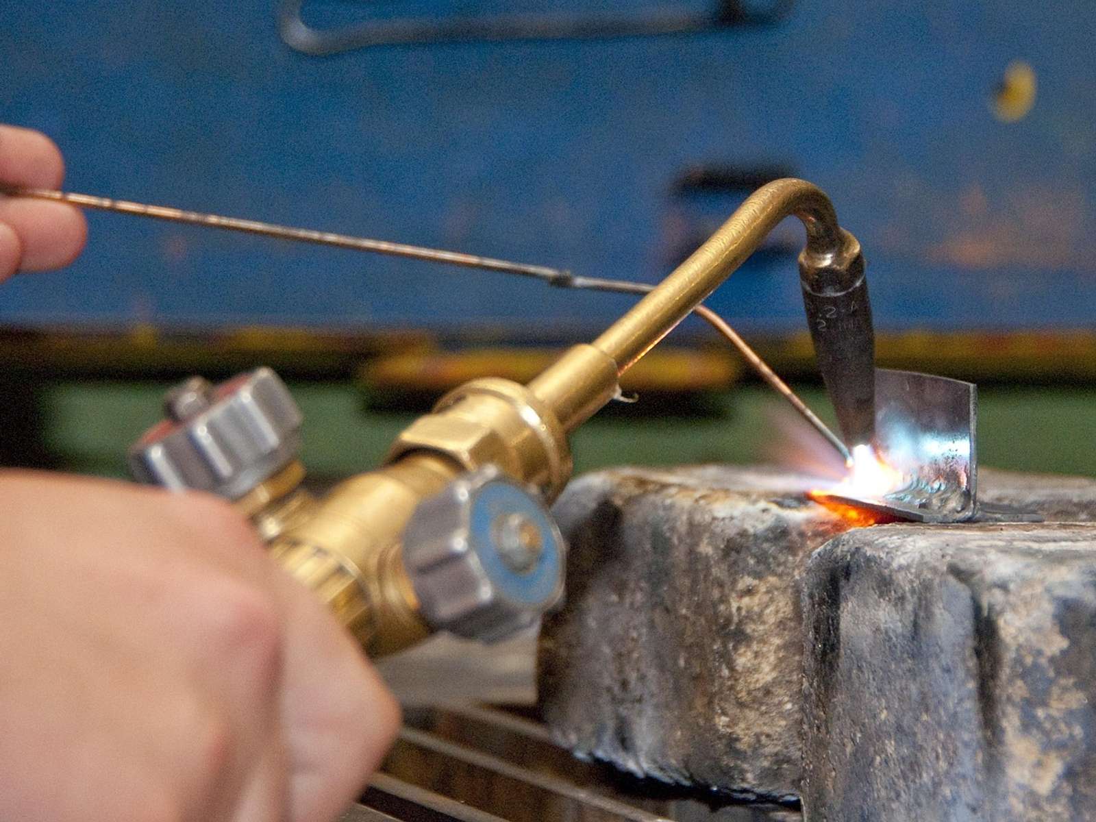 A hand holding a gas torch over a piece of metal in a workshop