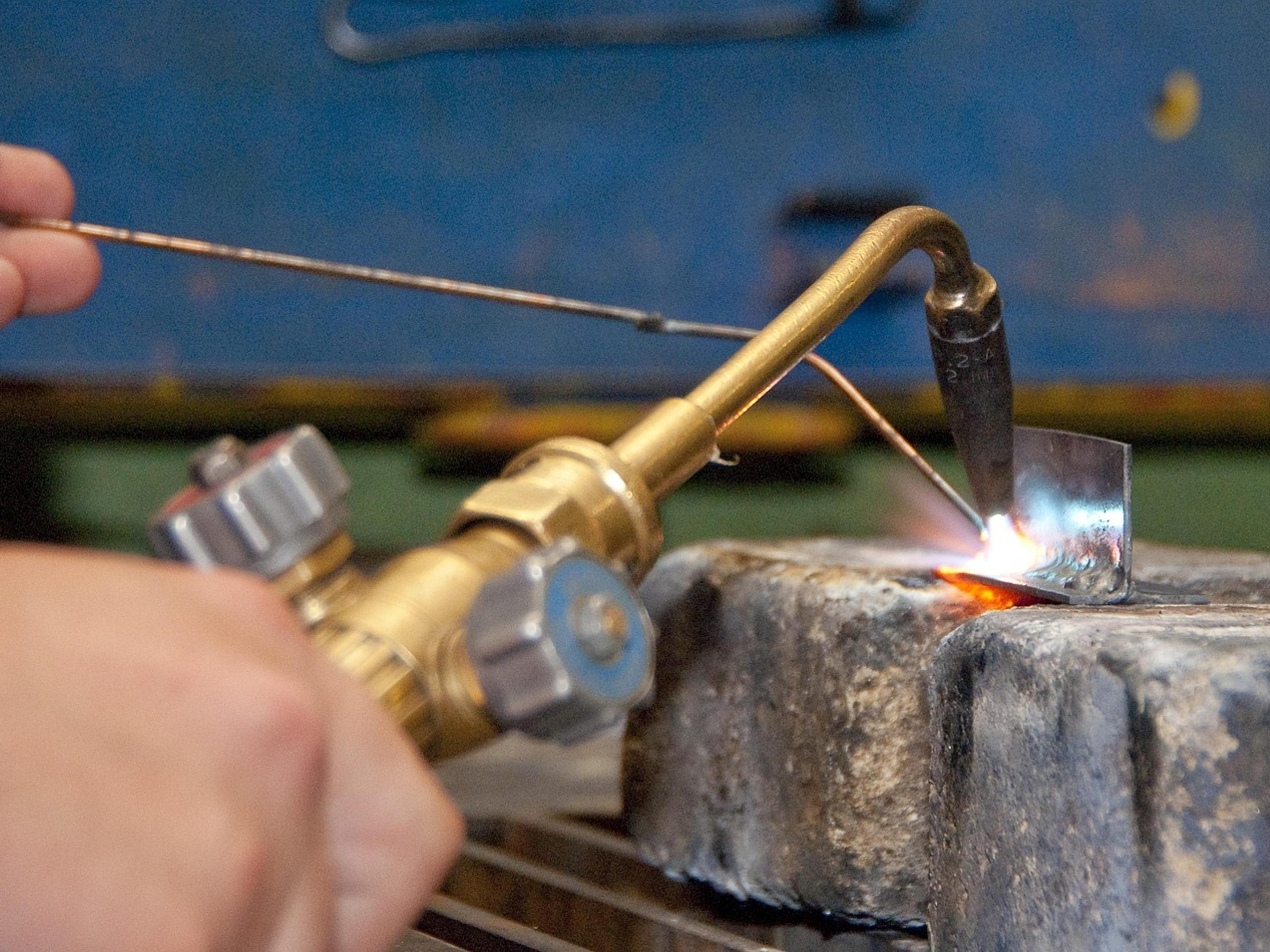 A hand holding a gas torch over a piece of metal in a workshop