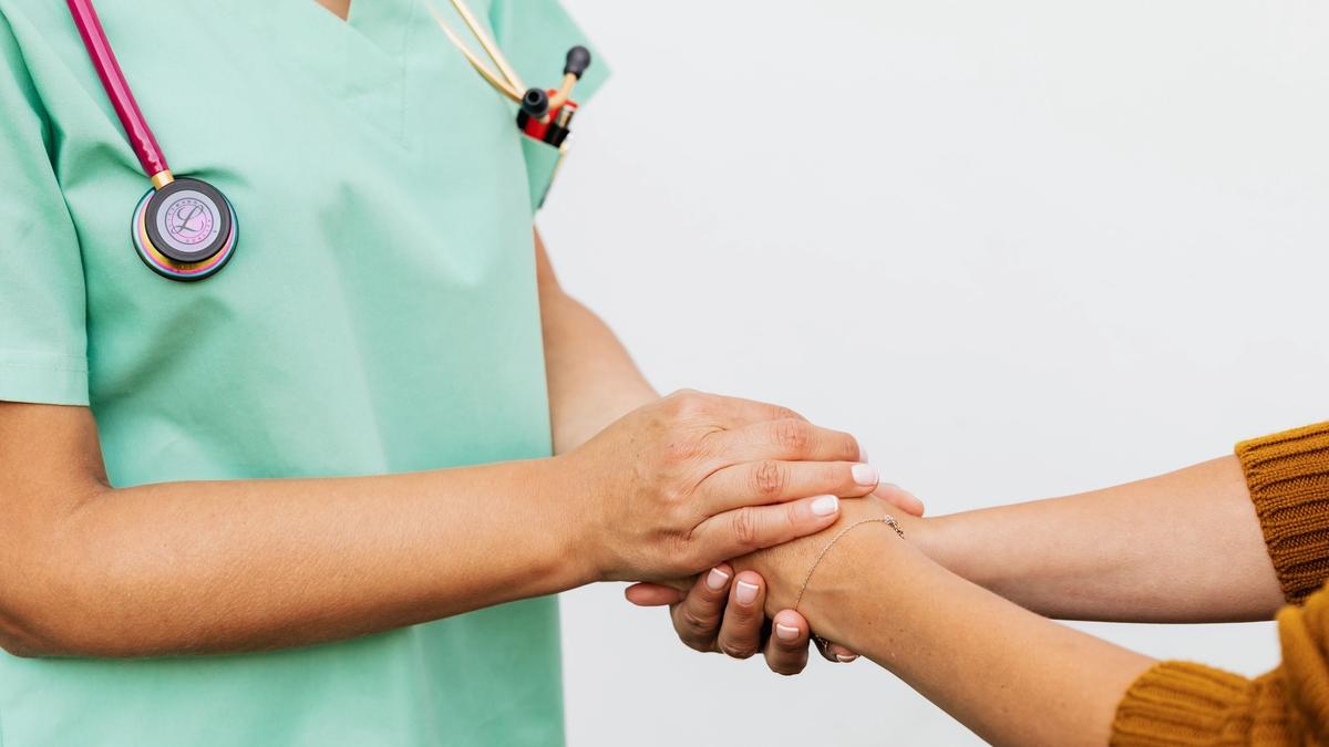 A nurse in green scrubs gently holding a patient's hand and wrist in a comforting gesture.