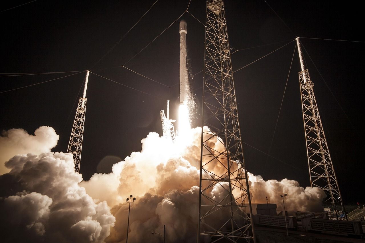 A rocket lifting off at night in a cloud of exhaust beside its launch towers
