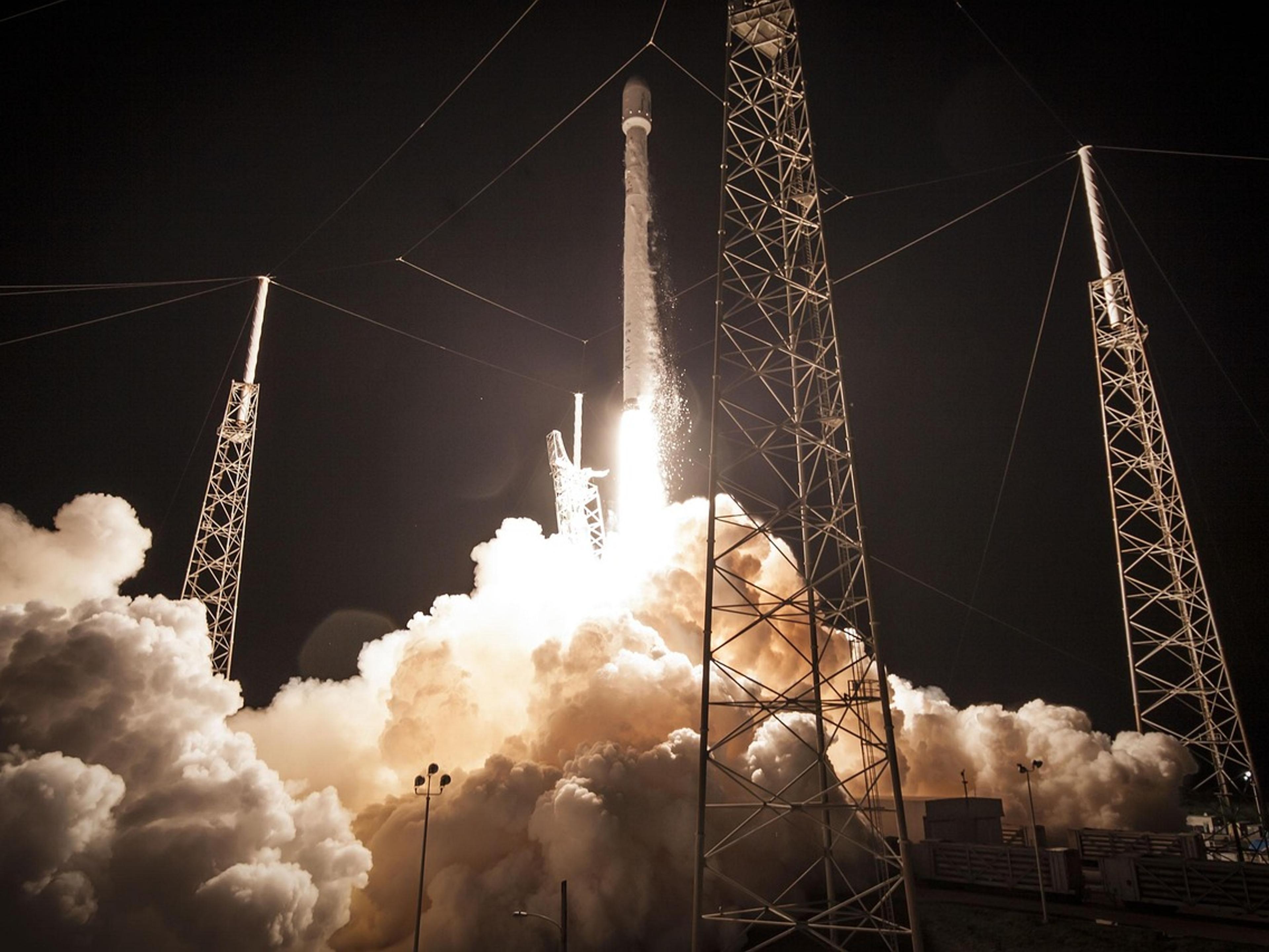 A rocket lifting off at night in a cloud of exhaust beside its launch towers
