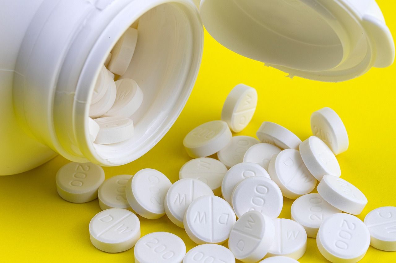White tablets spilling out of an open medicine bottle onto a yellow surface