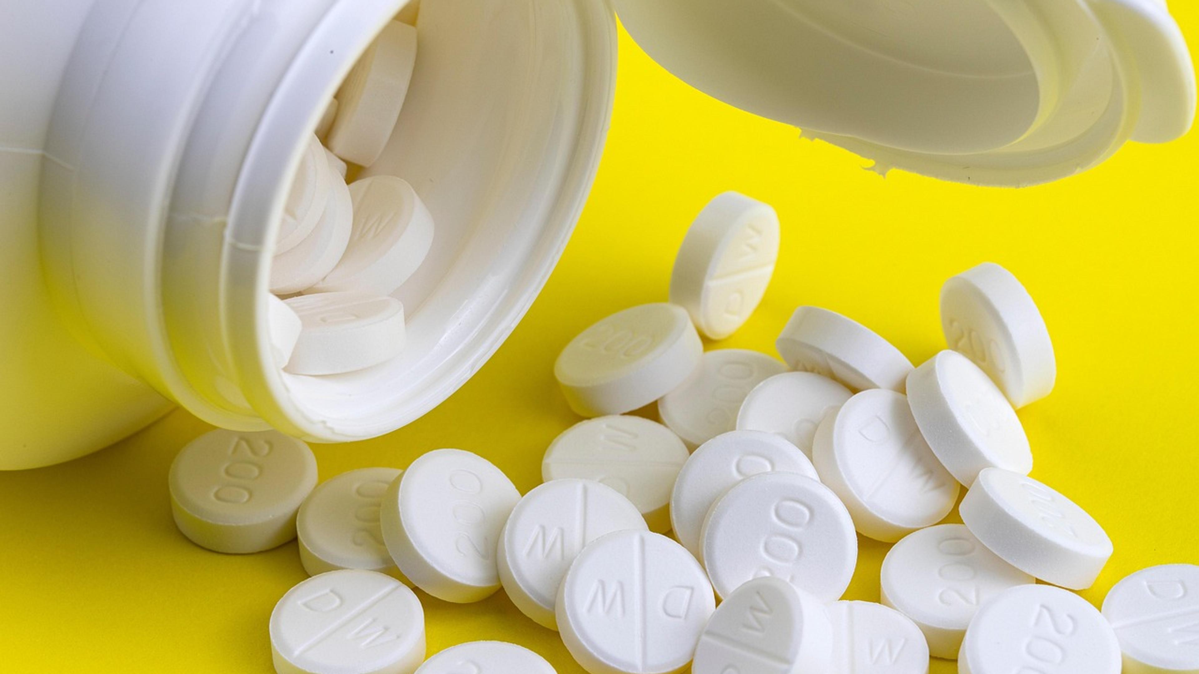 White tablets spilling out of an open medicine bottle onto a yellow surface