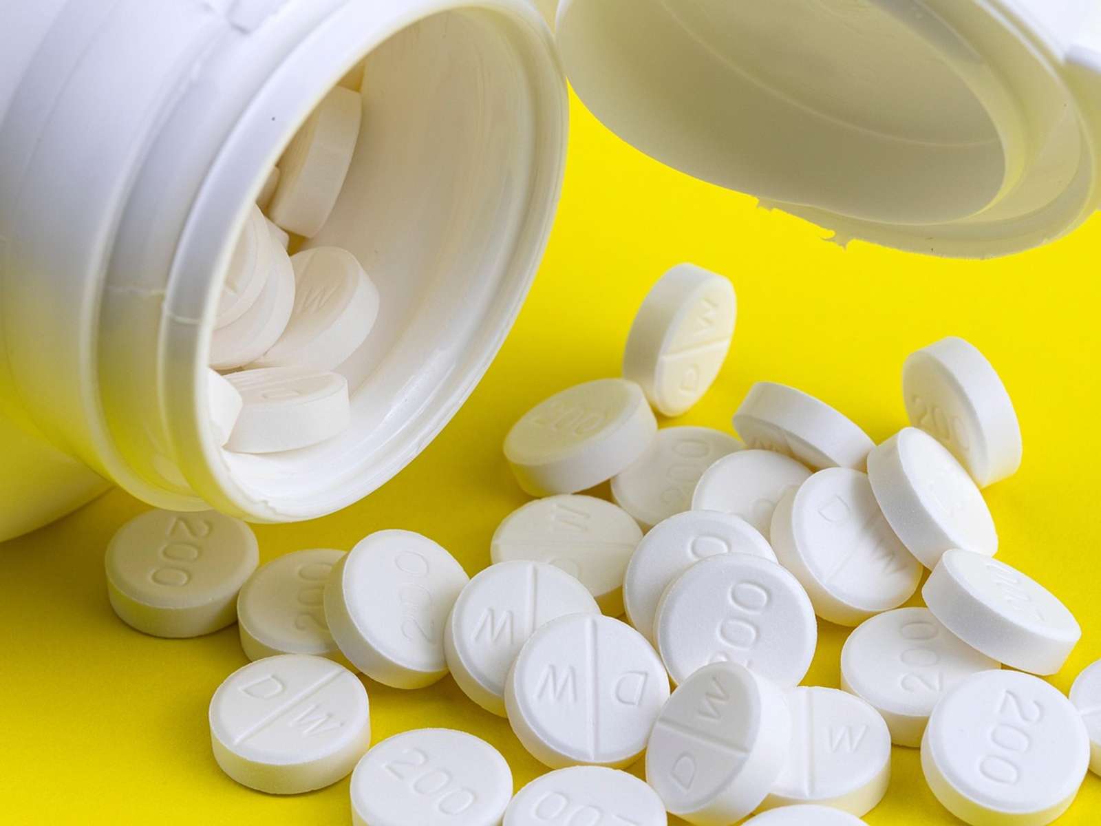 White tablets spilling out of an open medicine bottle onto a yellow surface