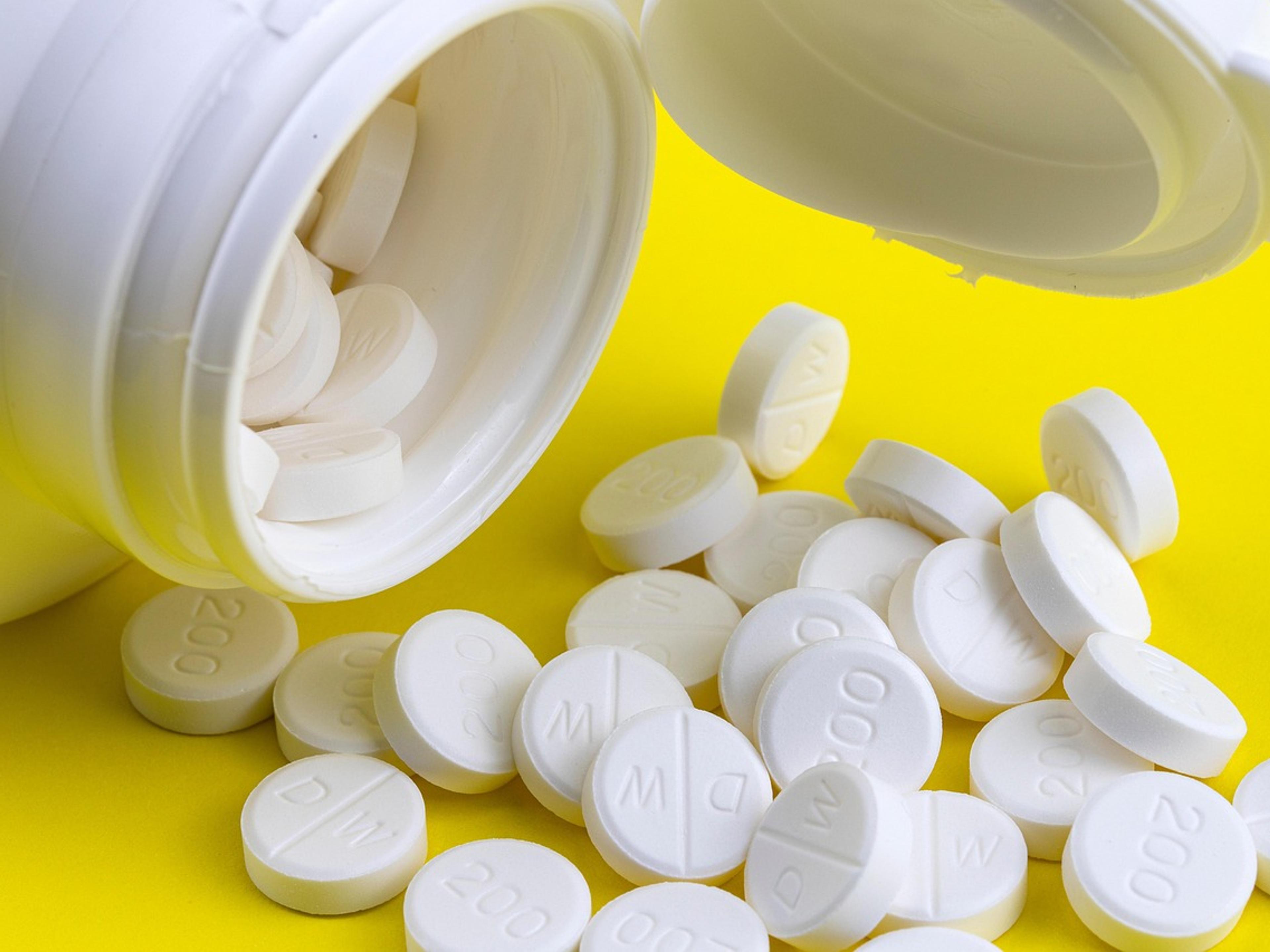 White tablets spilling out of an open medicine bottle onto a yellow surface