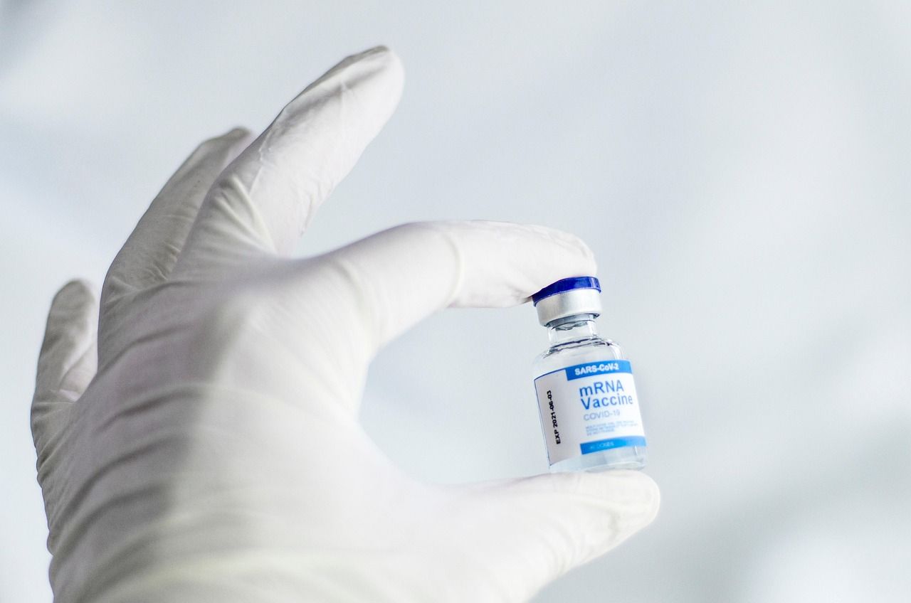A gloved hand holding a small glass vaccine vial