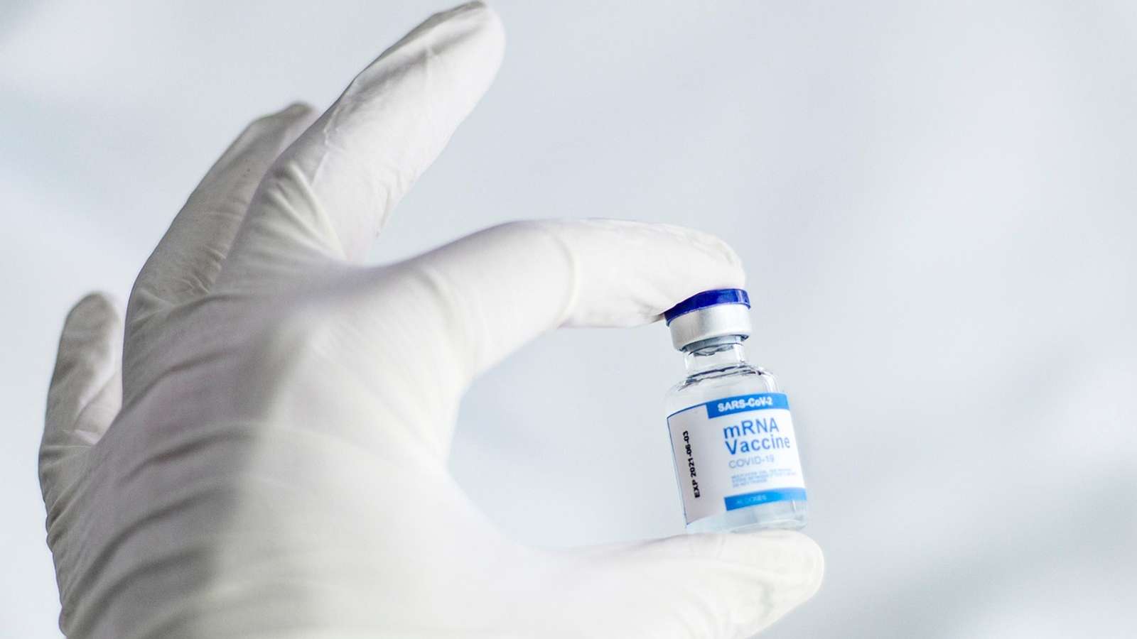 A gloved hand holding a small glass vaccine vial