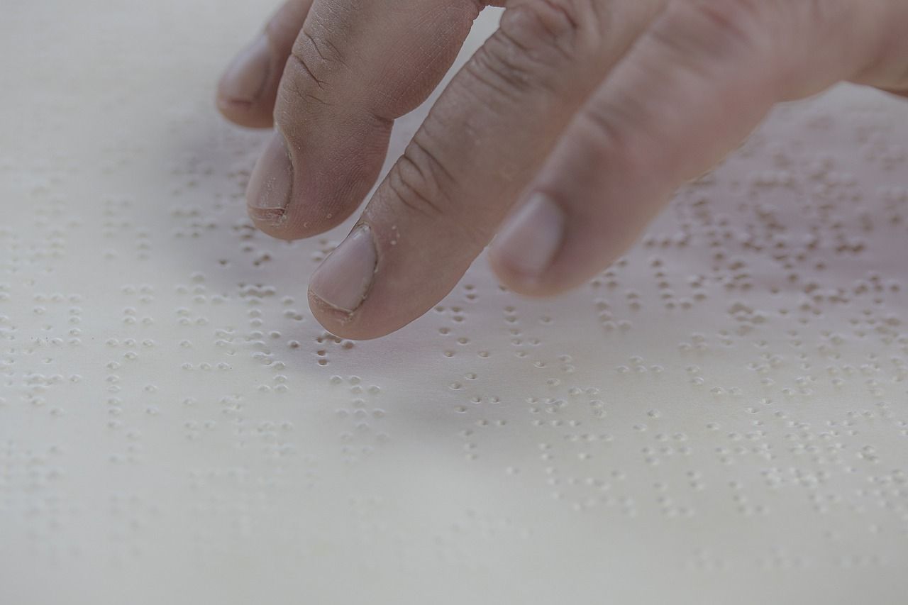 Fingers reading raised Braille dots on a white page