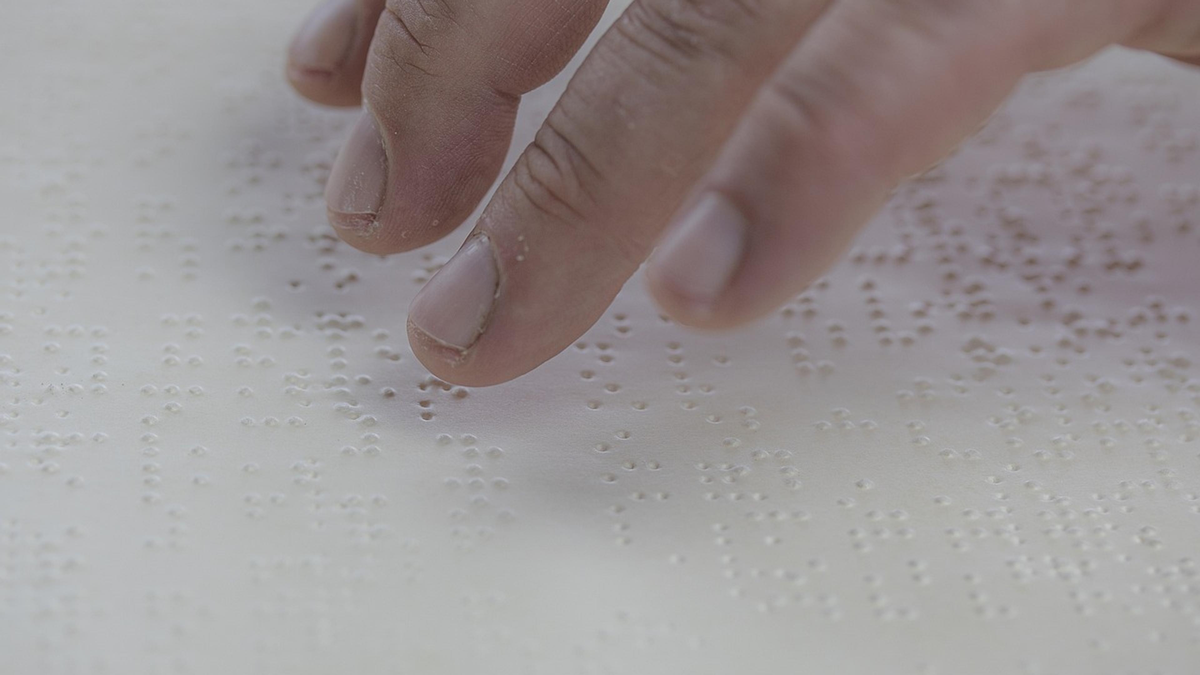 Fingers reading raised Braille dots on a white page