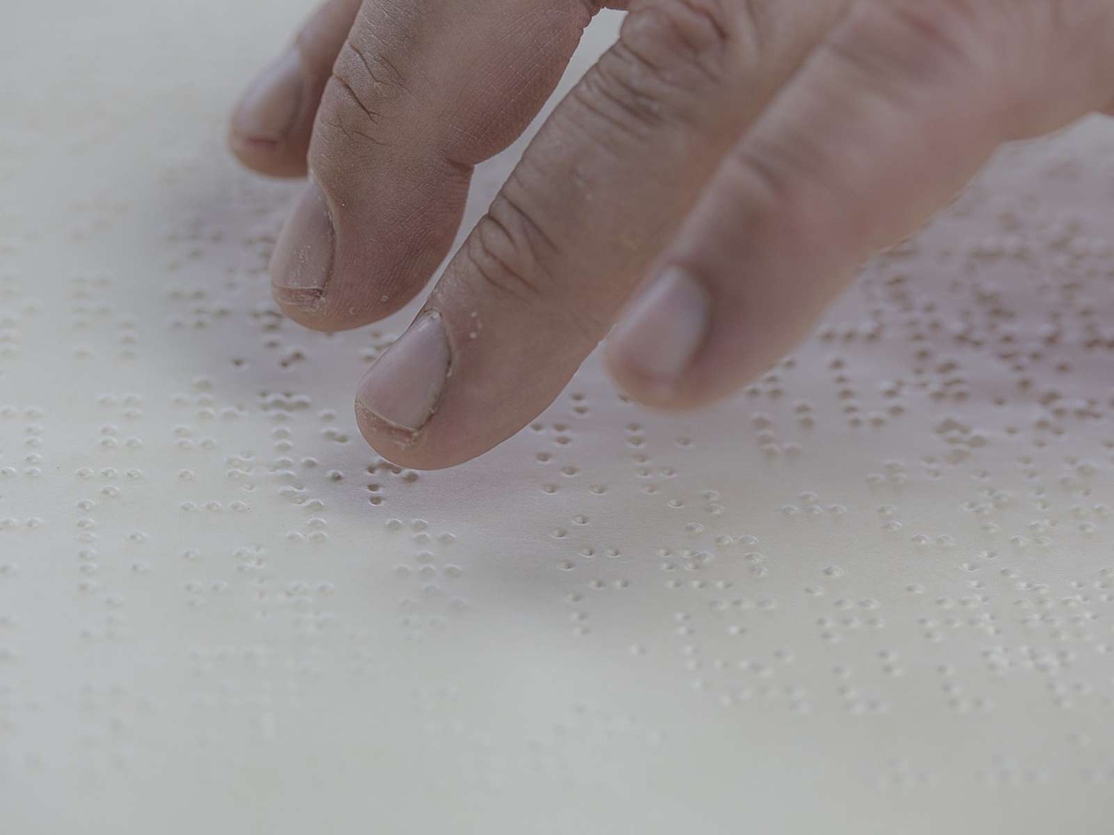 Fingers reading raised Braille dots on a white page