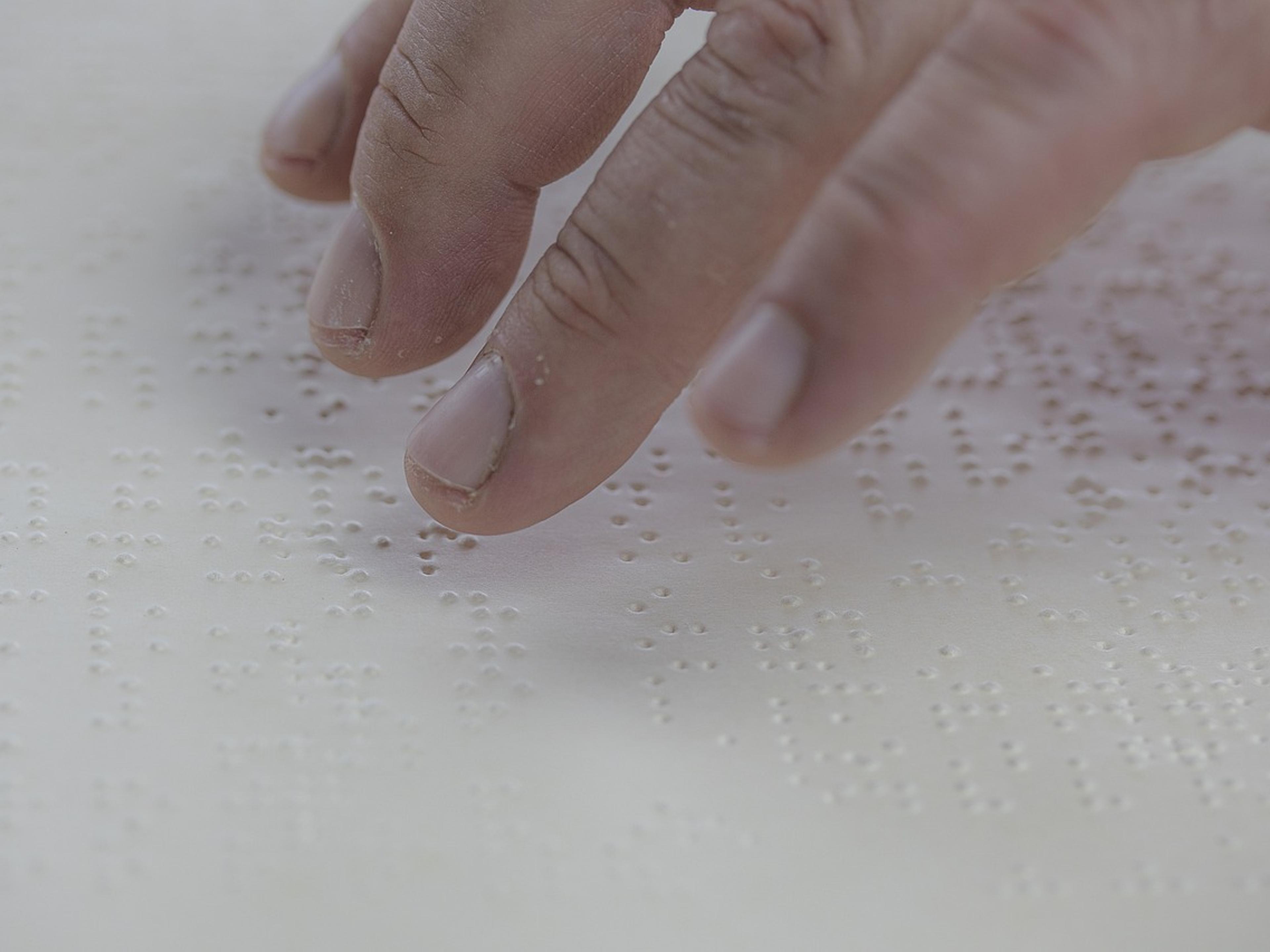 Fingers reading raised Braille dots on a white page