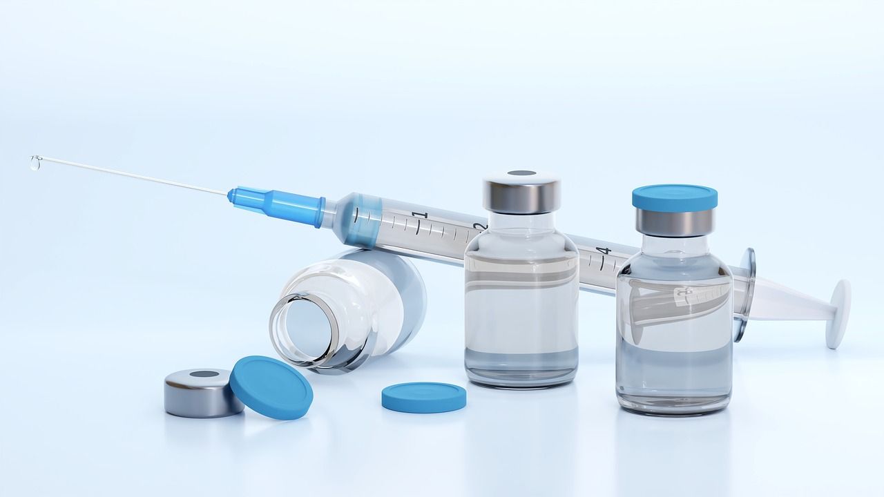 A syringe lying beside small glass vaccine vials on a white surface