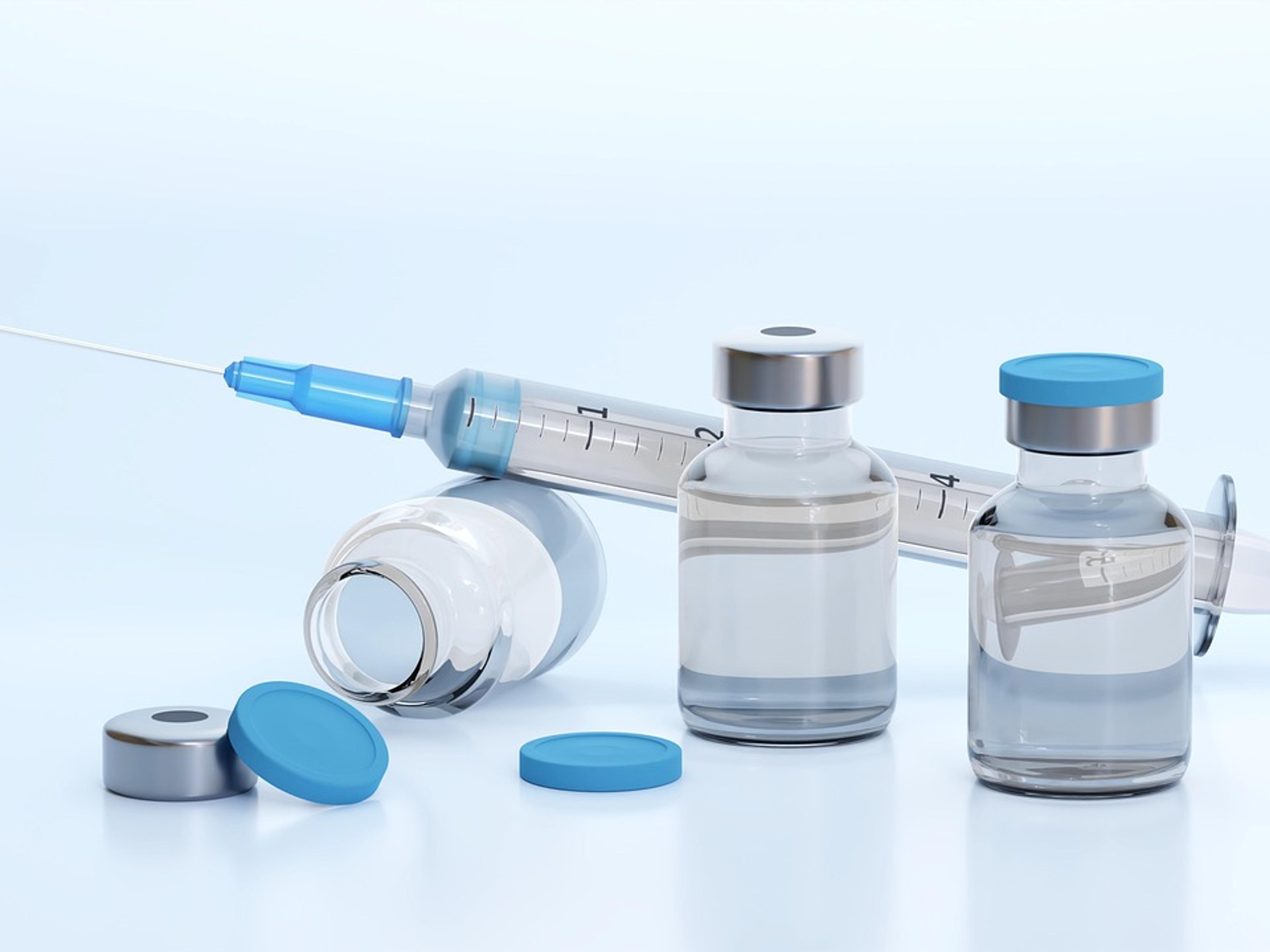 A syringe lying beside small glass vaccine vials on a white surface